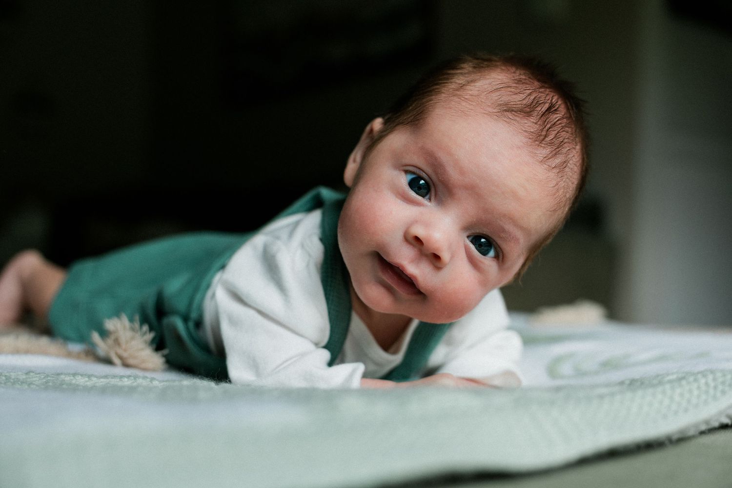 Adorable newborn baby with blue eyes doing tummy time on a soft blanket.
