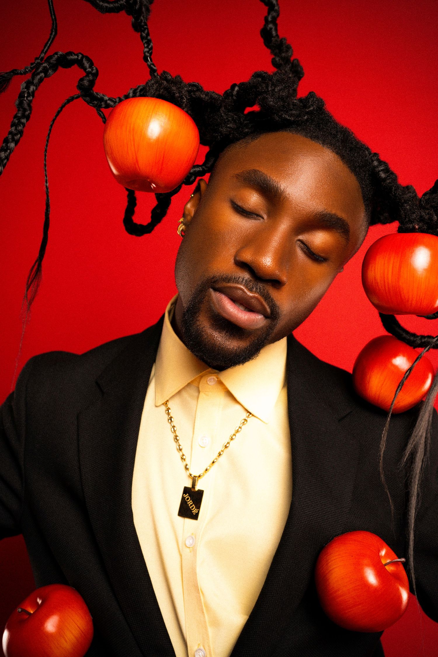 Creative portrait with red apples and black braids against crimson background.