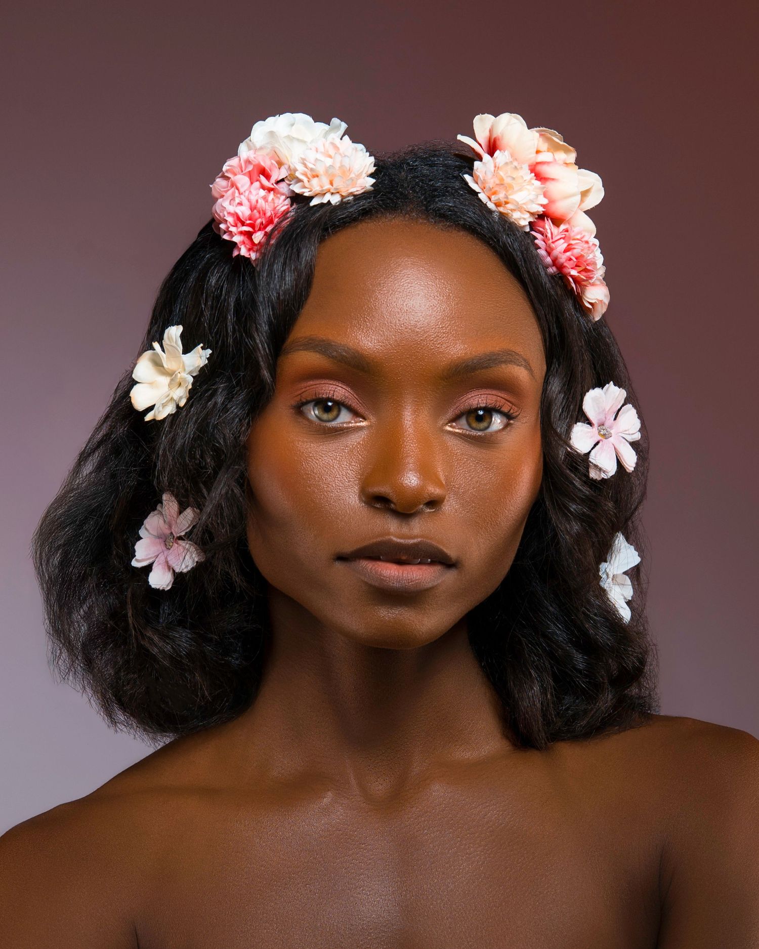 Romantic beauty portrait with delicate pink flowers in dark wavy hair.