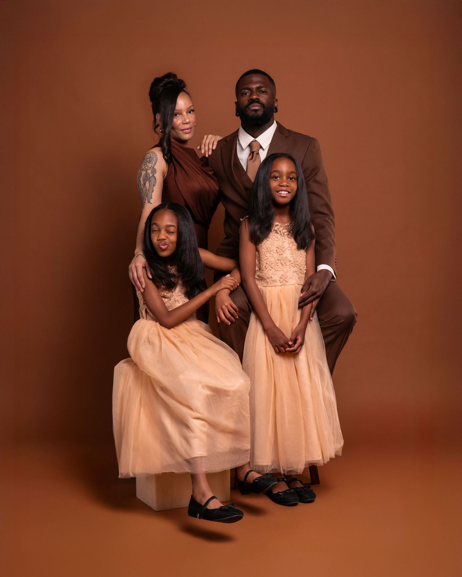 A family of four in coordinated brown and champagne outfits poses together for a professional portrait photo.