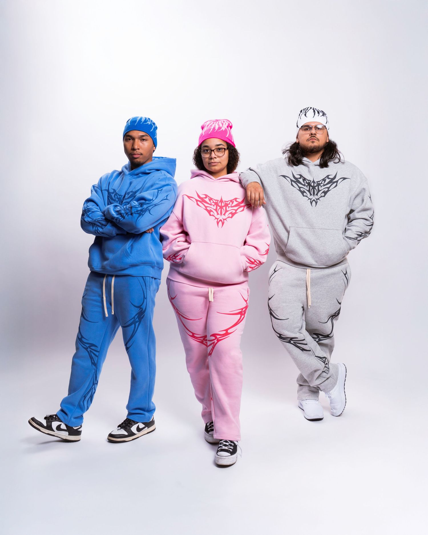 Three people in colorful puffy winter outfits - blue, pink, and gray - pose in different stances against a white backdrop.