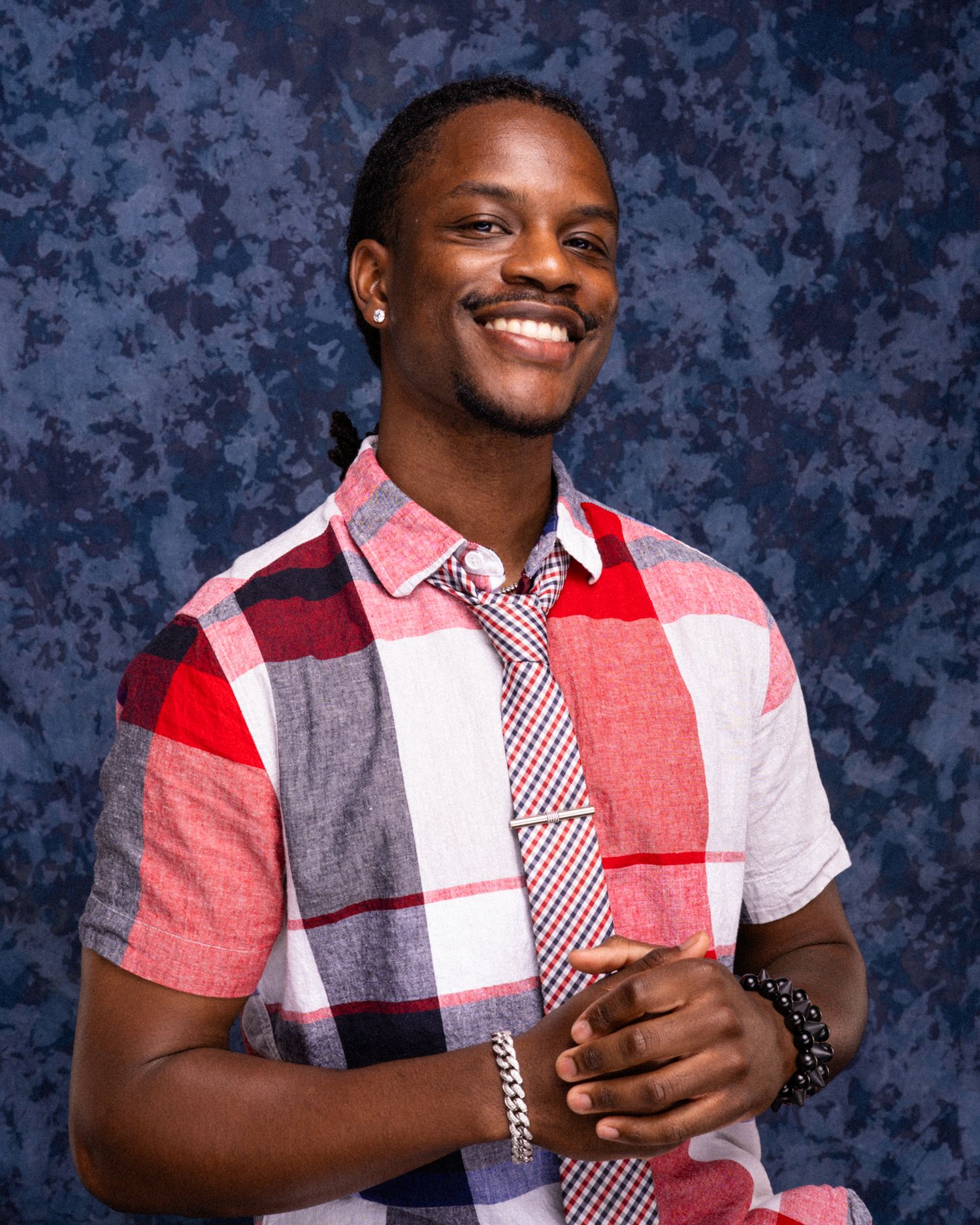 Smiling young man in red plaid shirt and tie poses for a professional portrait photo against blue background.