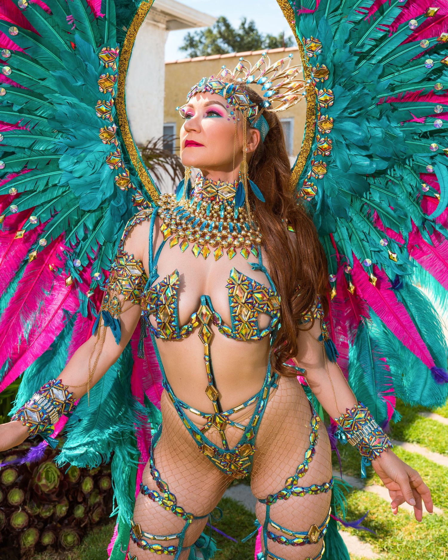 Ornate carnival costume with jeweled details and turquoise-pink feathered wings in sunlit garden.