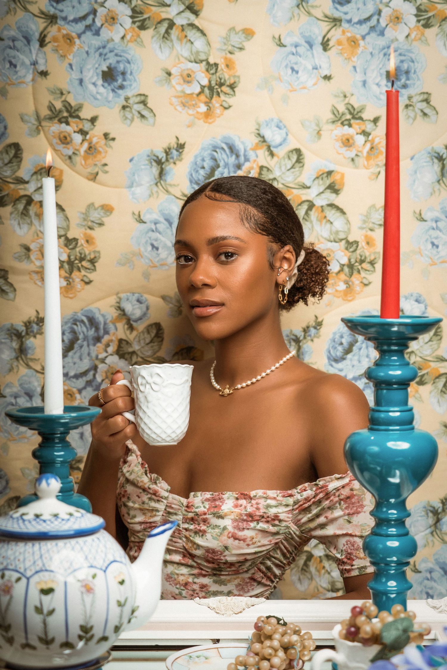 Elegant tea scene with person holding white teacup against floral wallpaper.