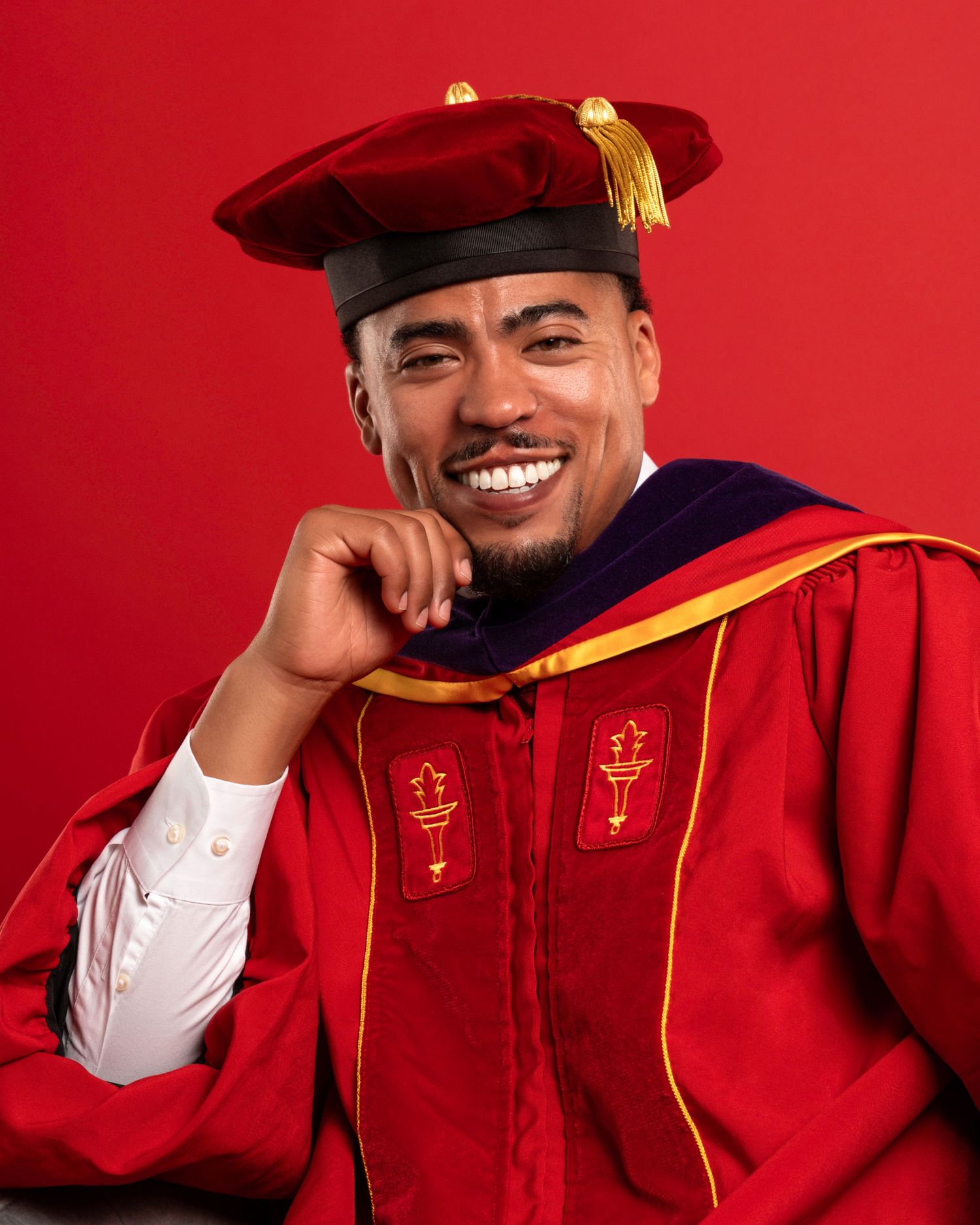 Graduate in red academic regalia and cap posing against a vibrant red background.