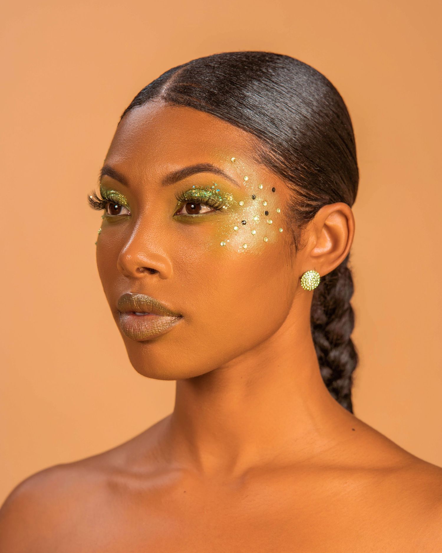 Glamour beauty shot with sparkly eye makeup and glossy lips on warm orange backdrop.