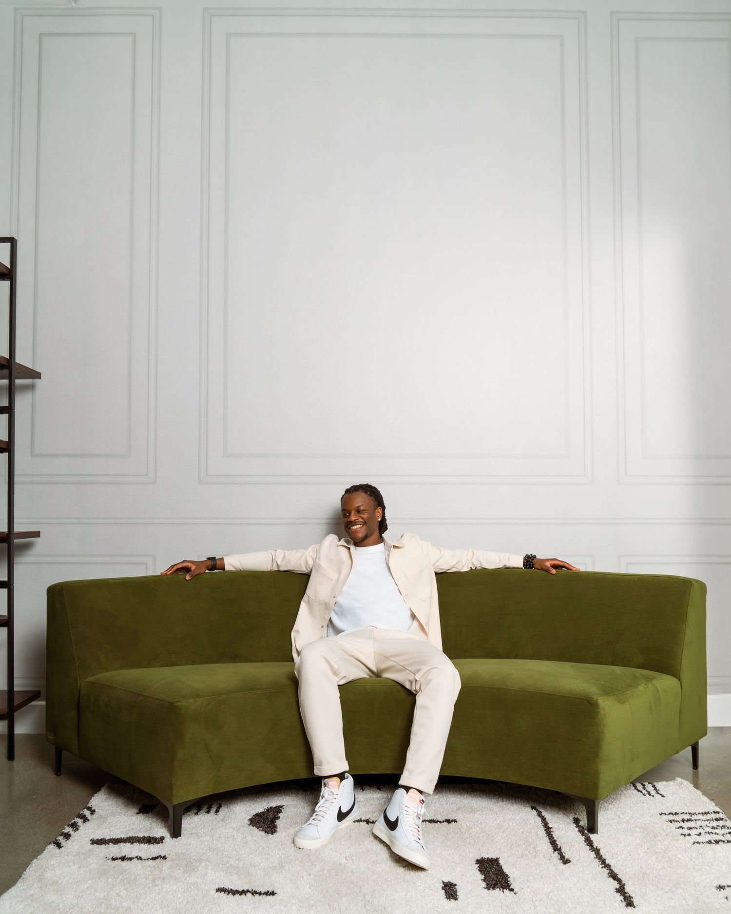 A person in white clothing sits and leans back on a green L-shaped couch against a white wall.
