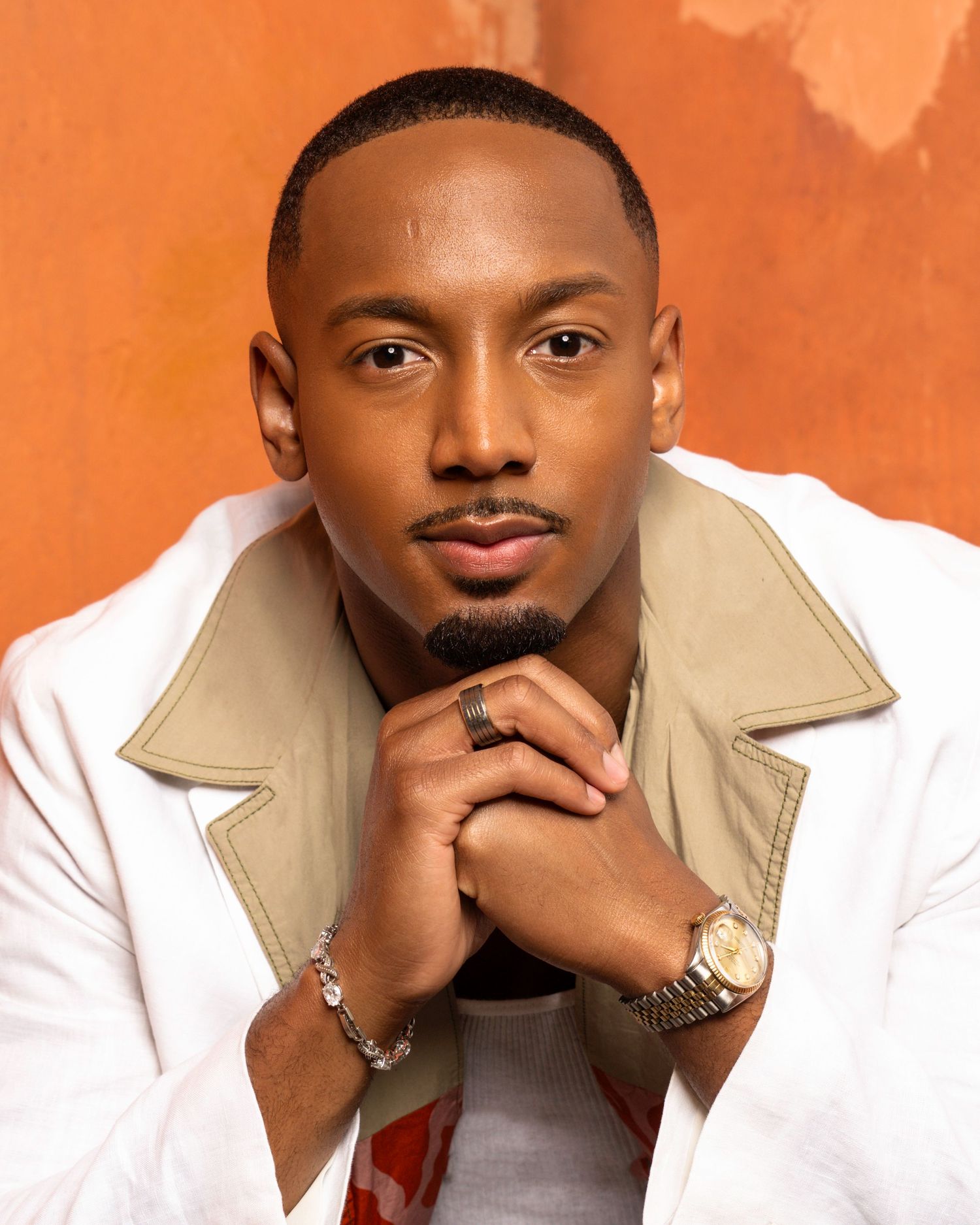 Portrait series against orange background wearing white jacket and beige collar.