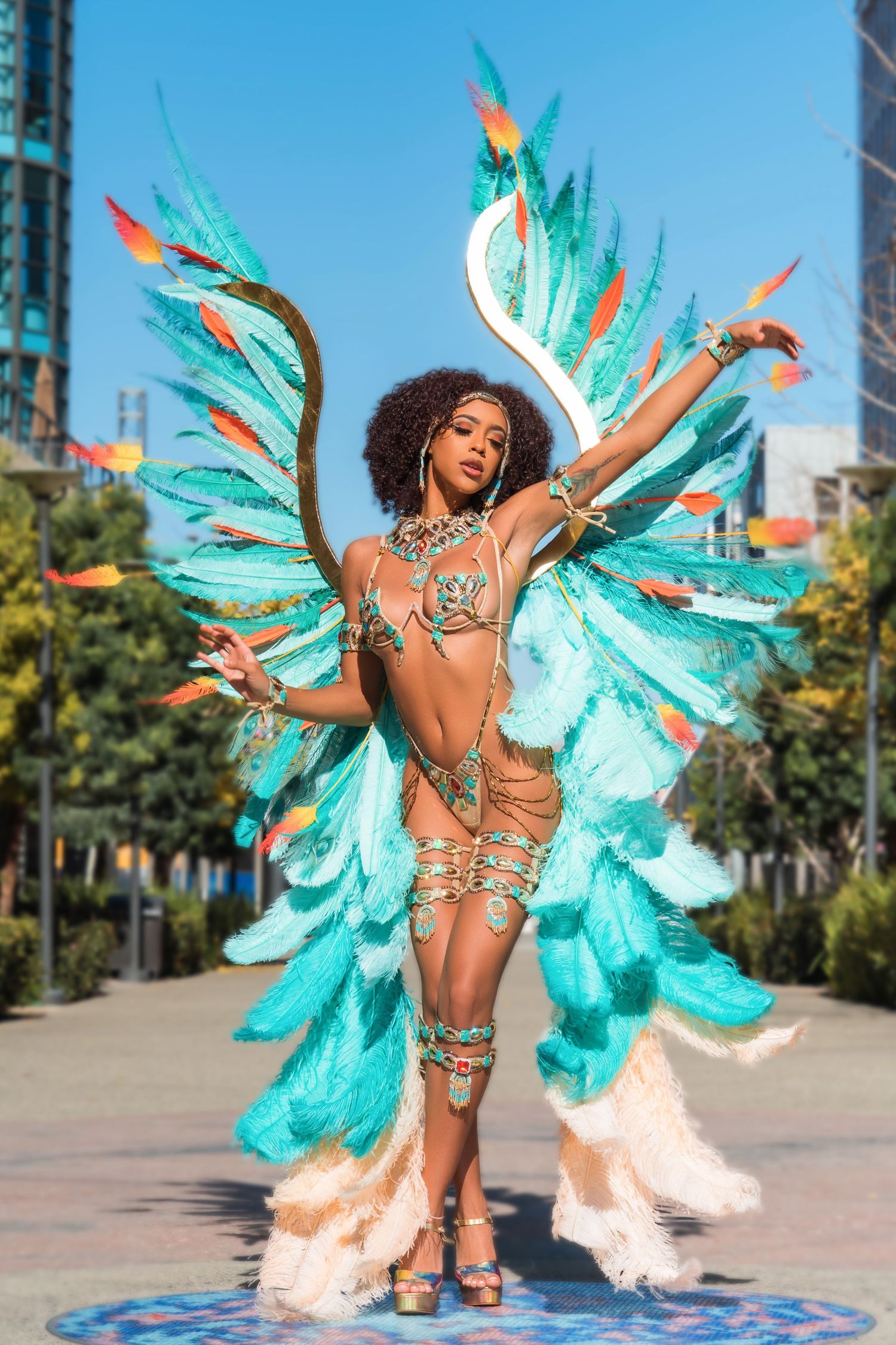 Energetic carnival dance performance with turquoise and white feathered wings in city plaza.