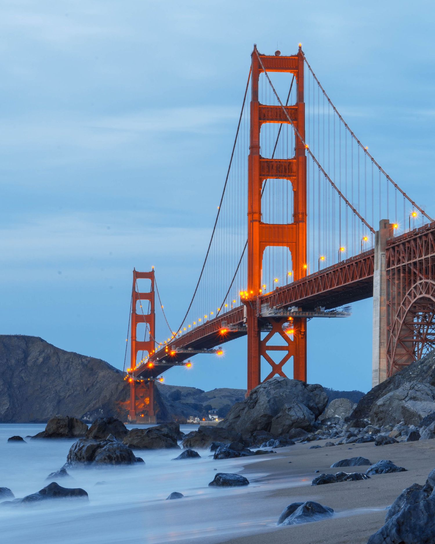 The iconic Golden Gate Bridge towers over a rocky beach during sunset in San Francisco, California.