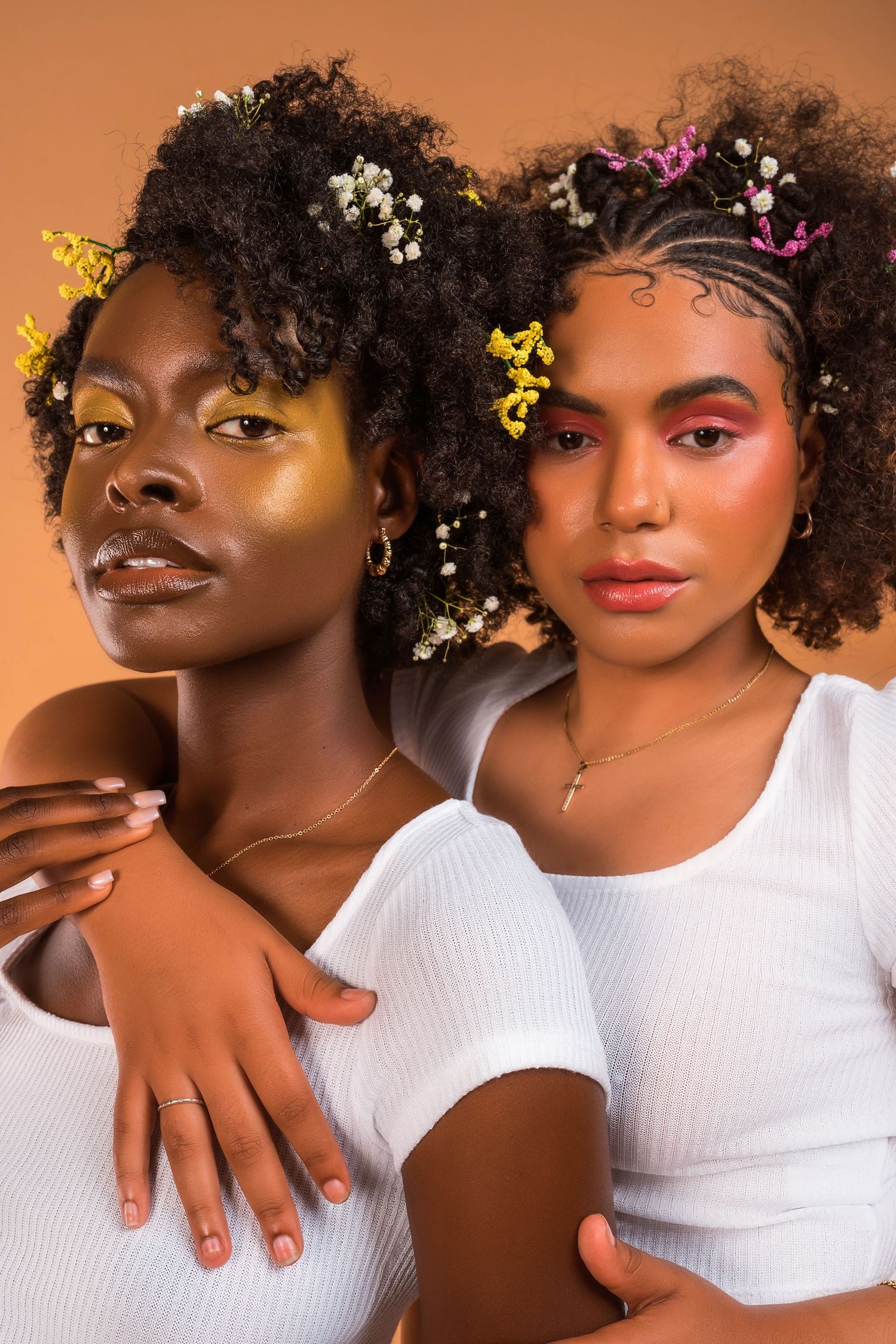 Models with floral hair accessories pose together in white tops against warm orange background.