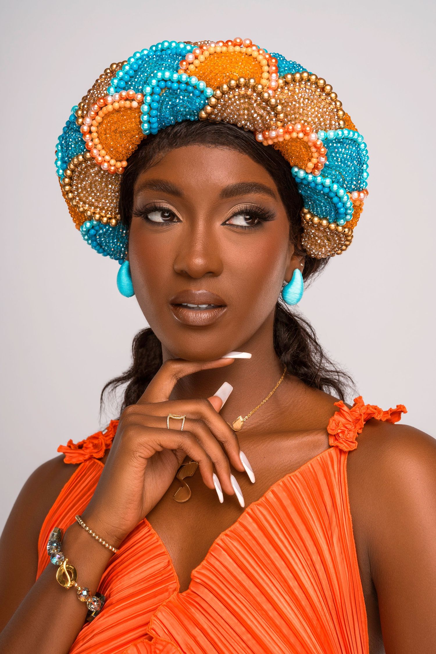 Fashion portrait in orange dress with ornate blue and gold beaded headpiece against white background.