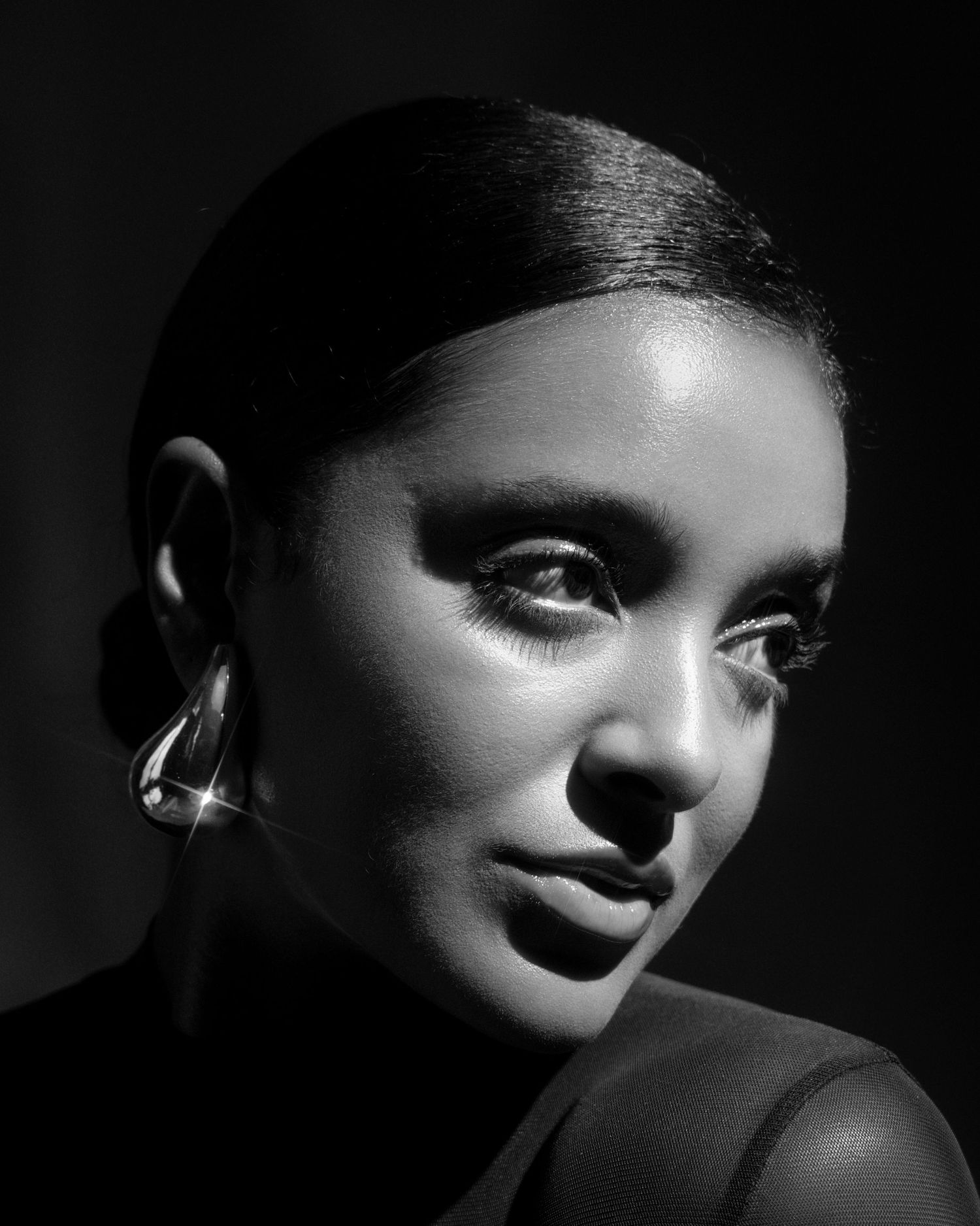 Dramatic black and white portrait with strong side lighting and metallic earrings.