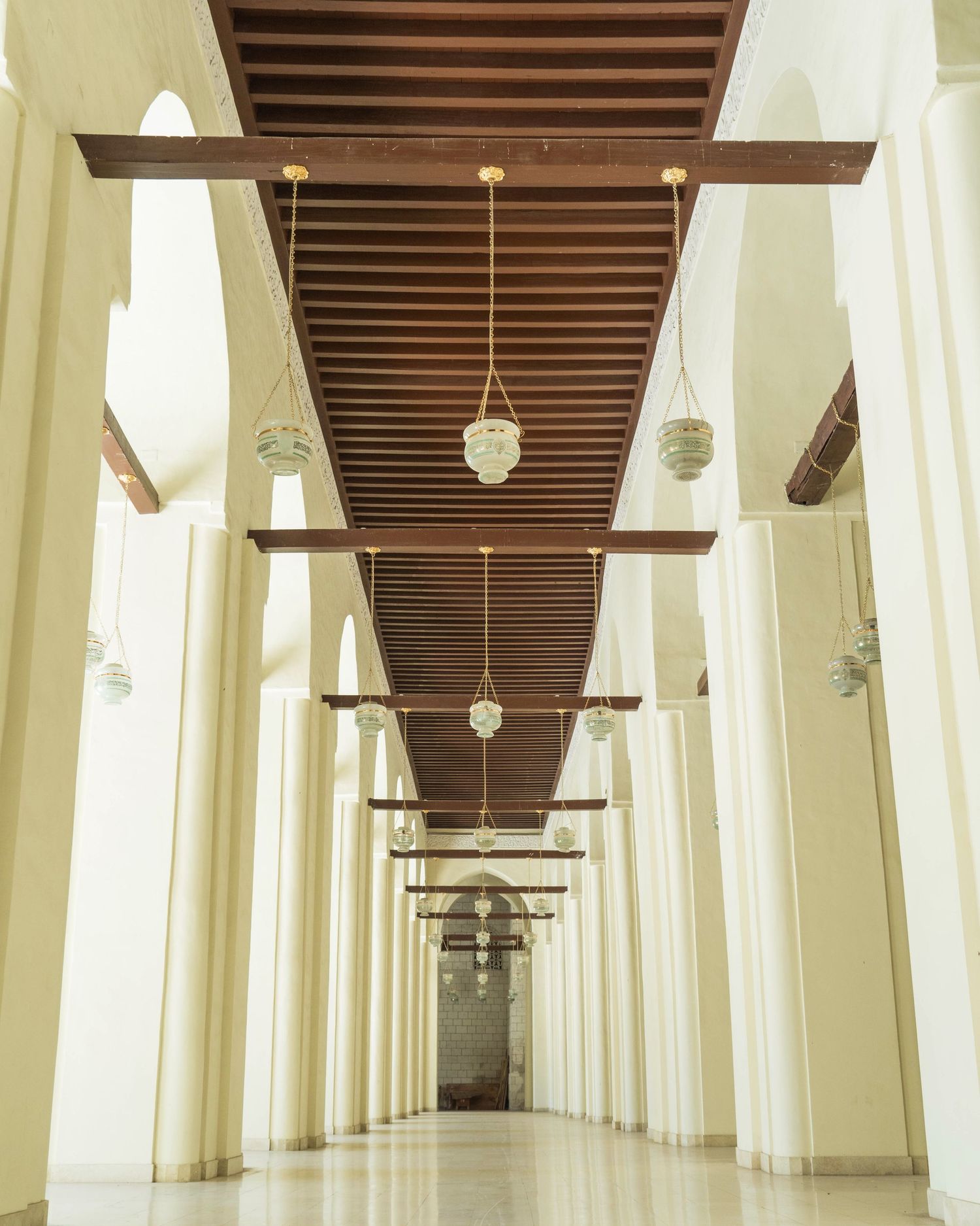 Long symmetrical corridor with white arches and wooden ceiling beams creating dramatic perspective.