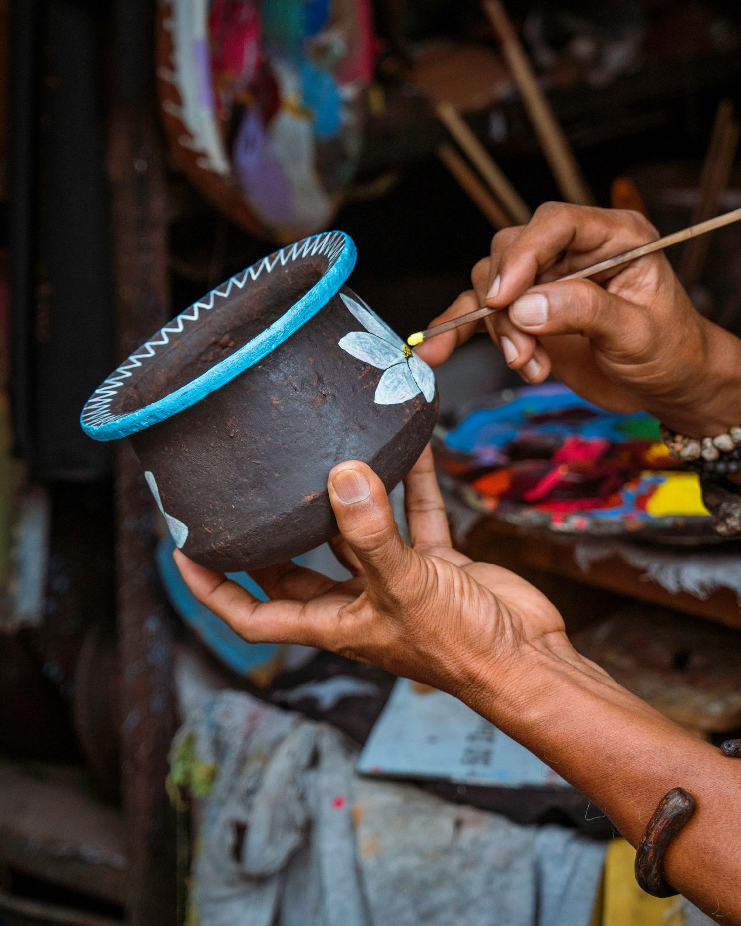Close-up of hands painting decorative details on a clay pot with blue trim.