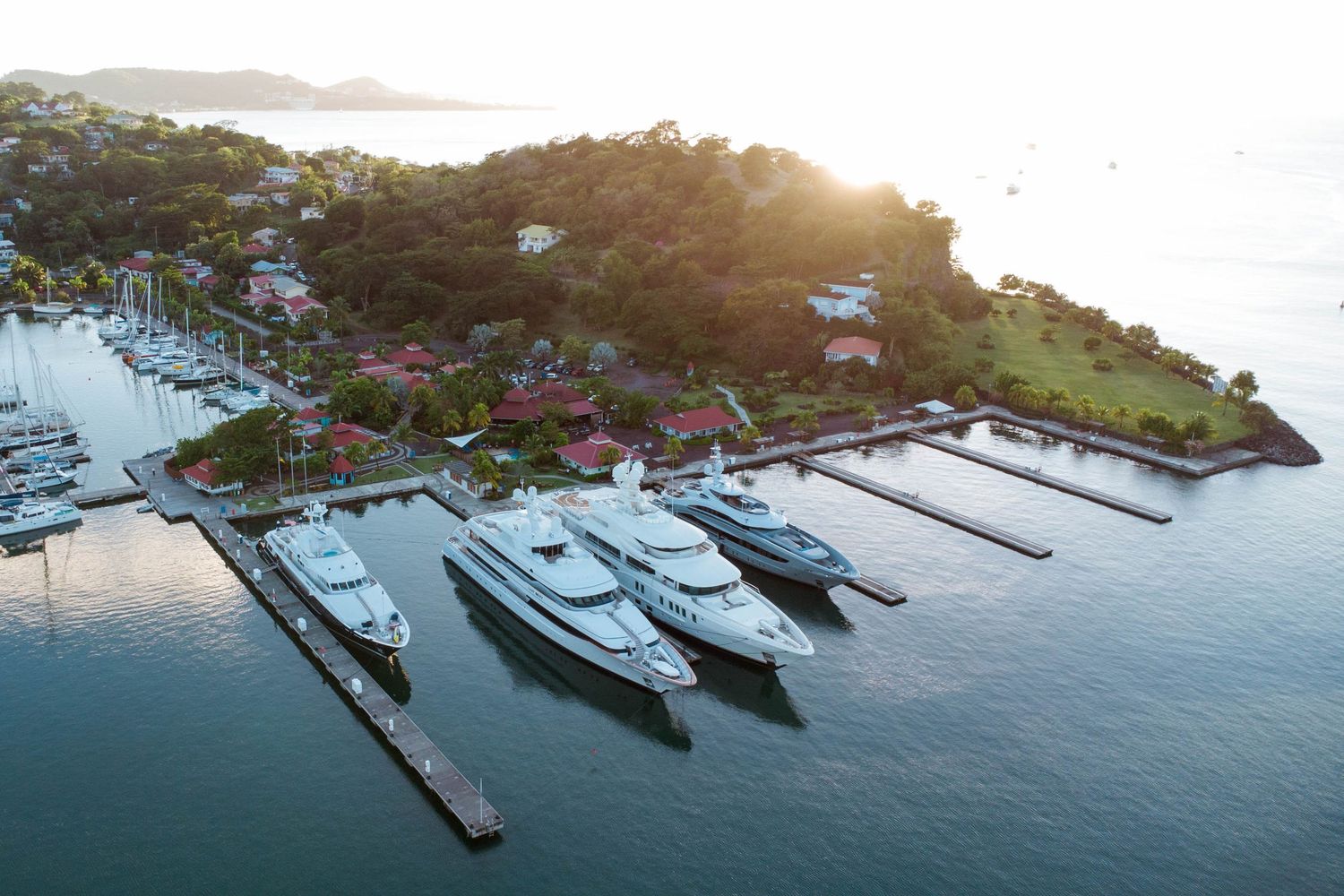 Aerial view of luxury yachts docked at a tropical marina during sunset.