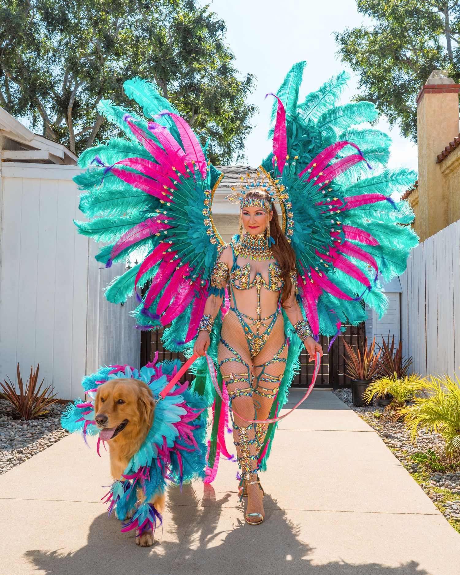 Vibrant turquoise and pink feathered carnival costumes displayed in an outdoor garden setting.