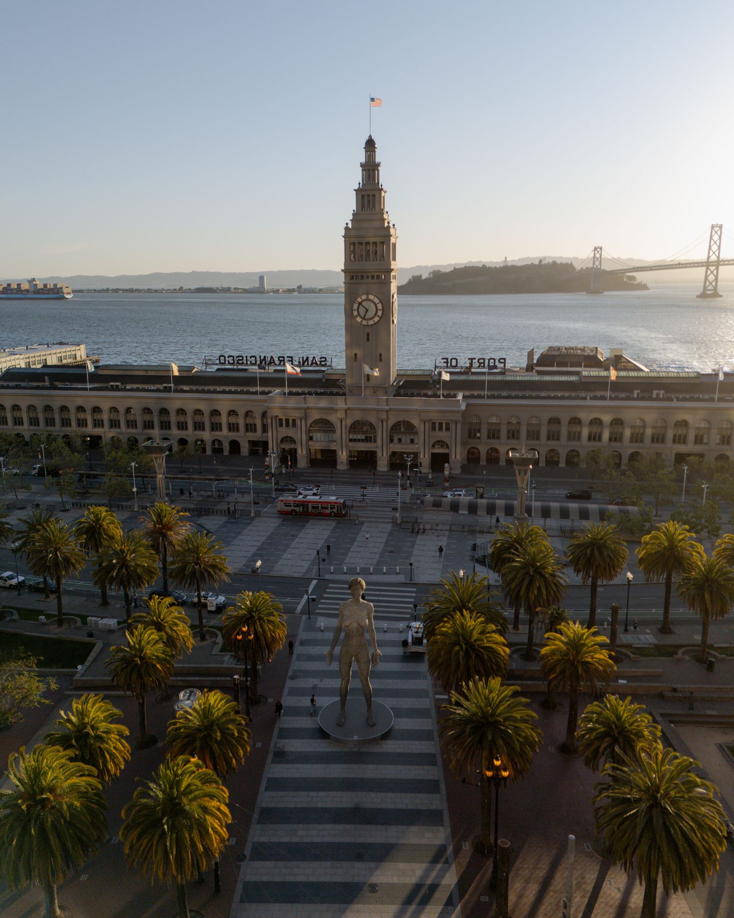 San Francisco Ferry Building plaza with palm trees and waterfront promenade at sunset.