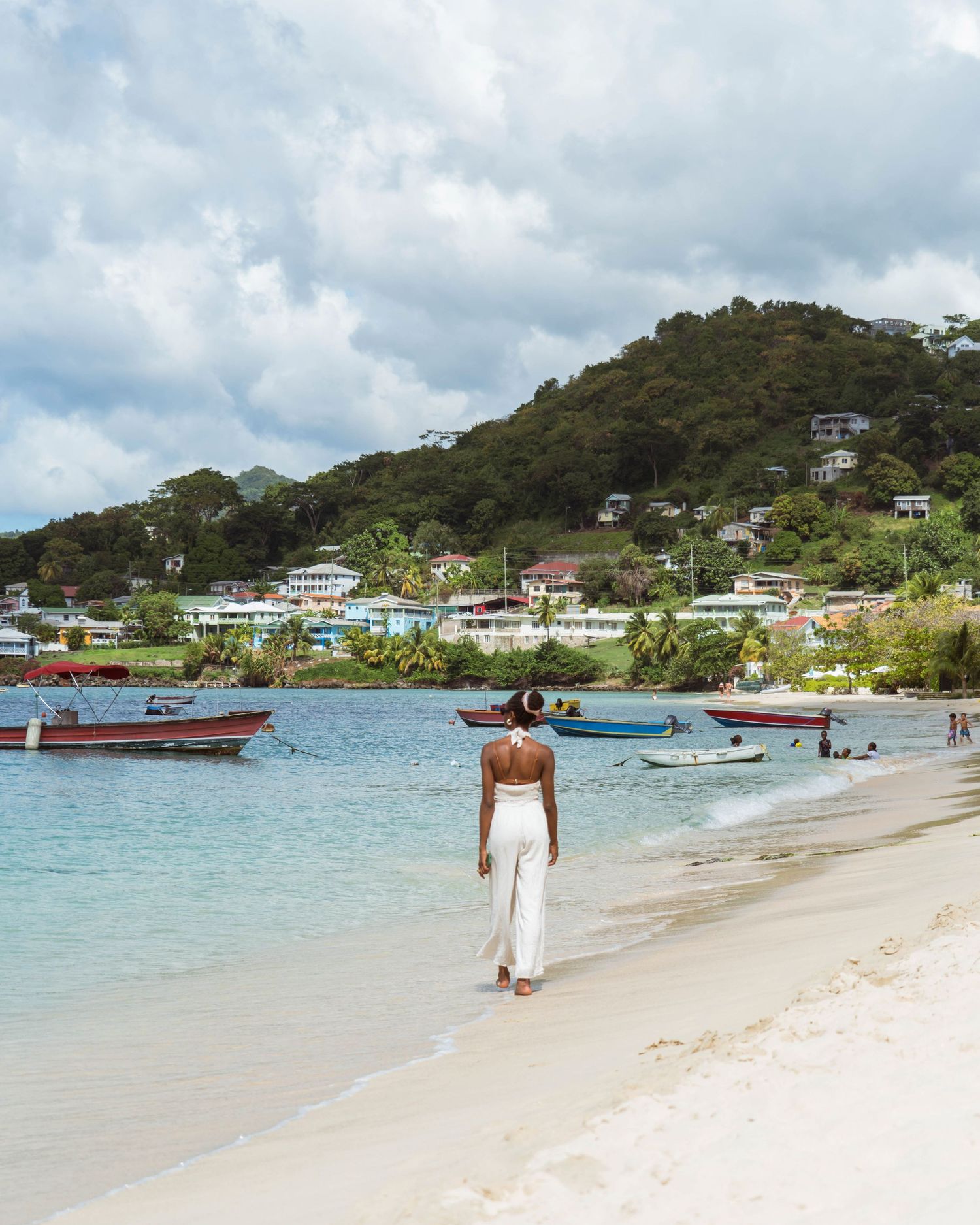 Scenic beach view with houses on hillside and boats in turquoise waters.