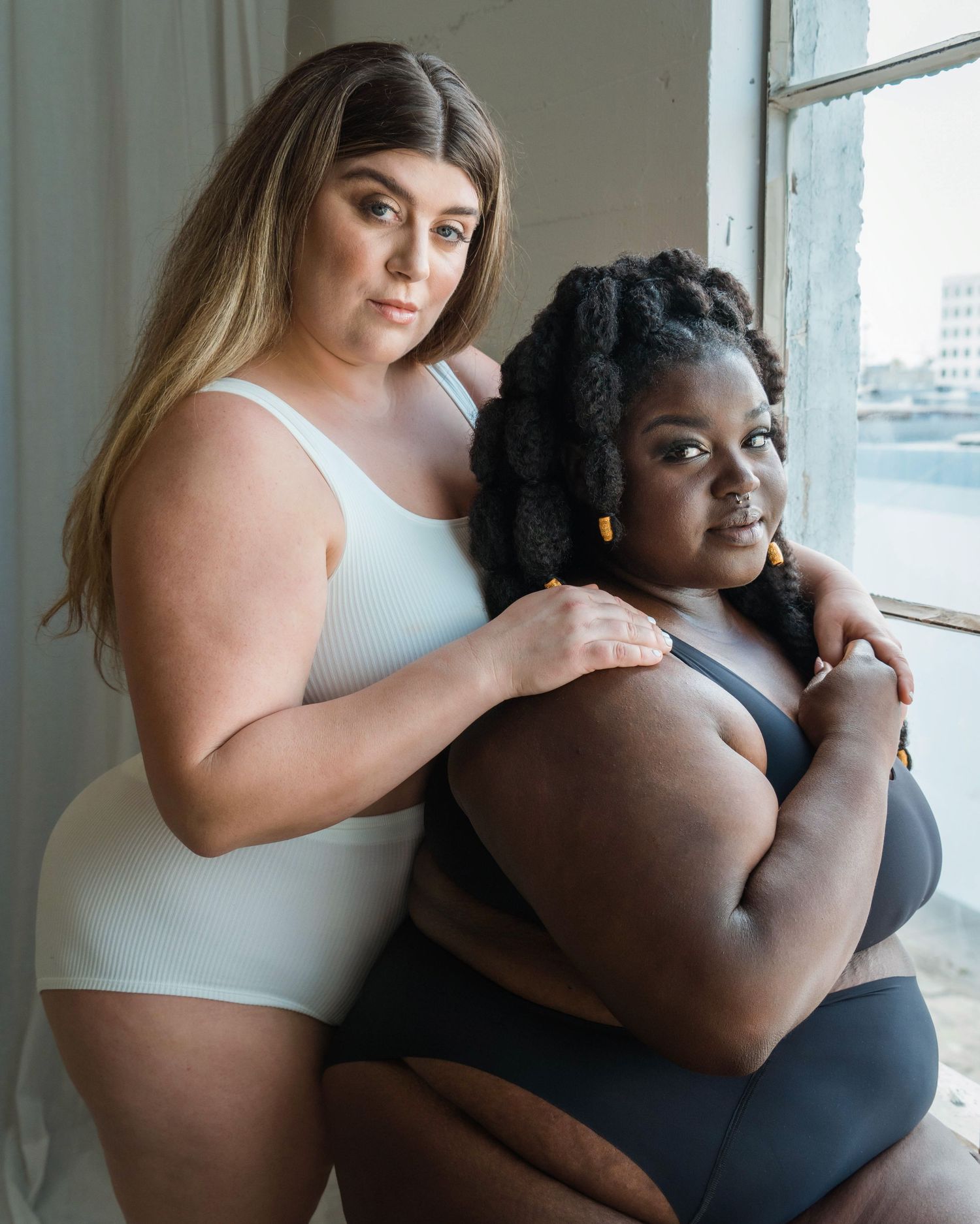 Intimate portrait series showing models embracing by window in contrasting outfits.