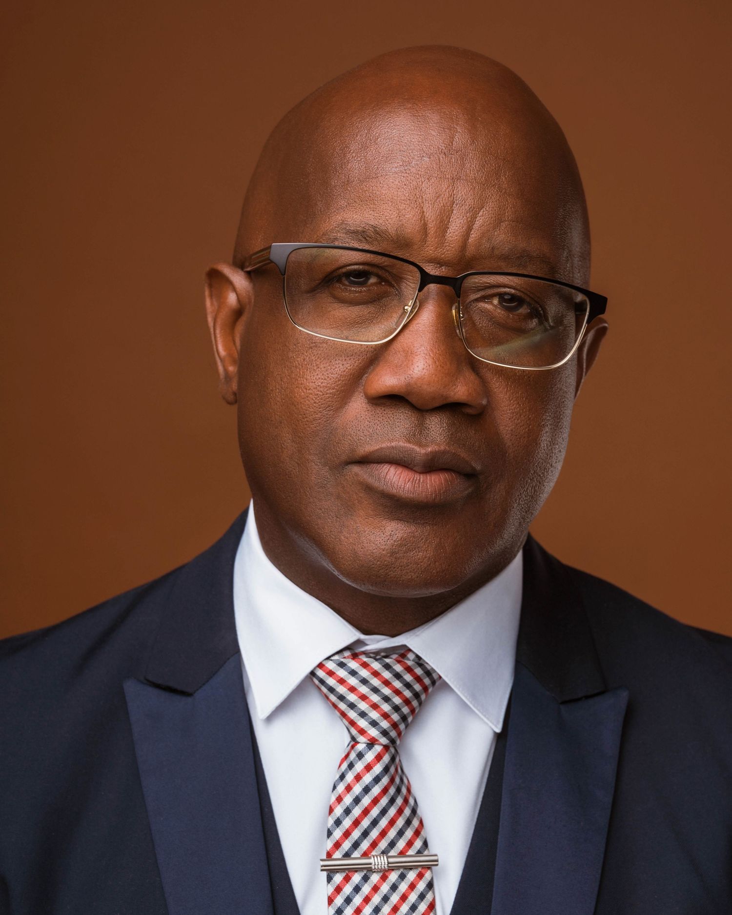 Professional headshots in business attire with striped tie against brown backdrop.