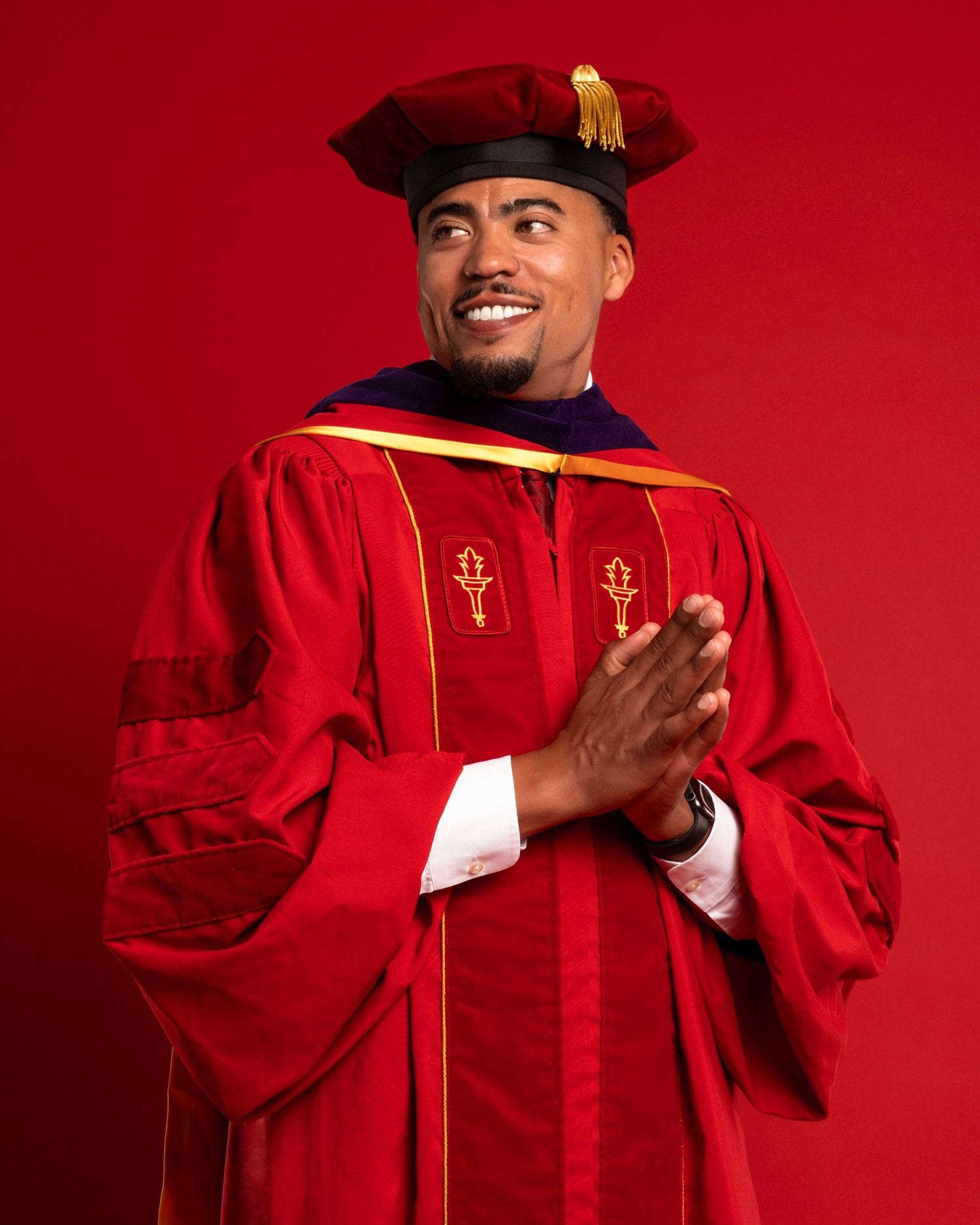 Academic graduate in bright red regalia making expressive poses against red backdrop.