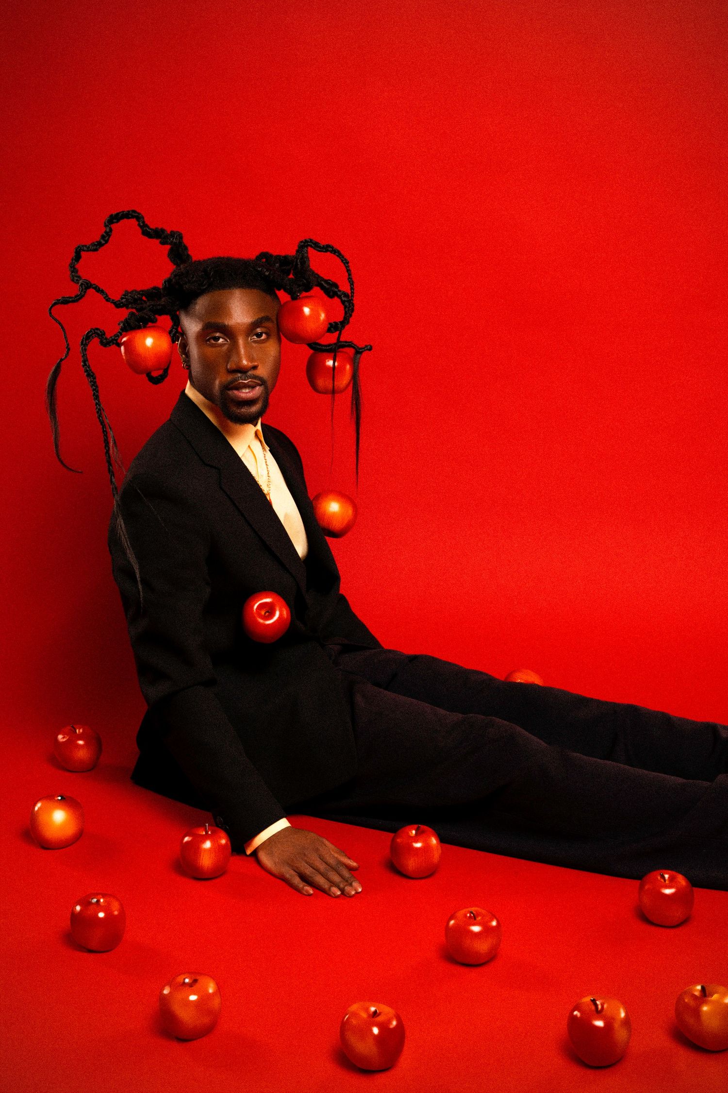 Stylish portrait with scattered red apples and braided hair while reclining on red floor.