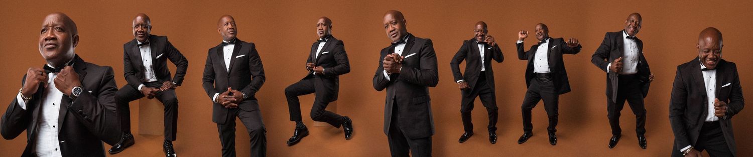Group portrait of performers in formal black attire against brown backdrop.
