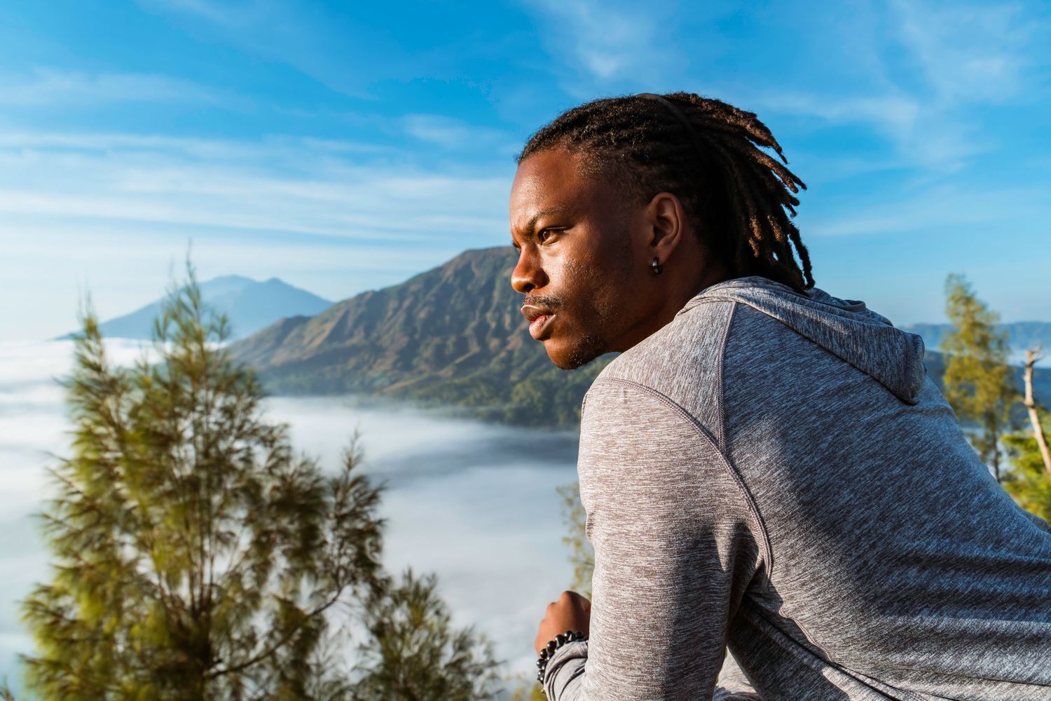 Person enjoying scenic mountain views while hiking through a misty forest landscape on a bright sunny day in Bali, Indonesia.