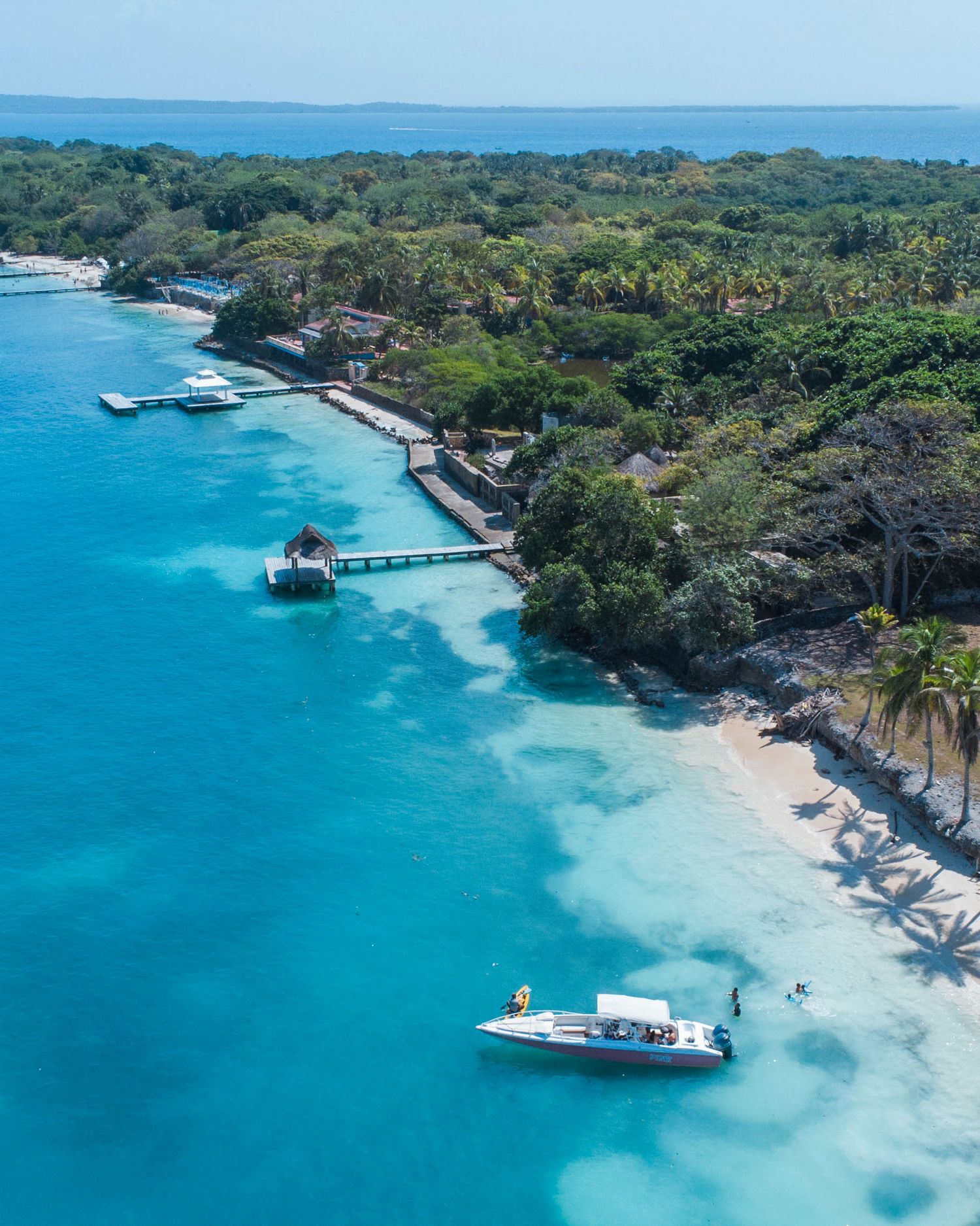 Aerial view of a tropical island beach with crystal clear turquoise waters and docked boats.