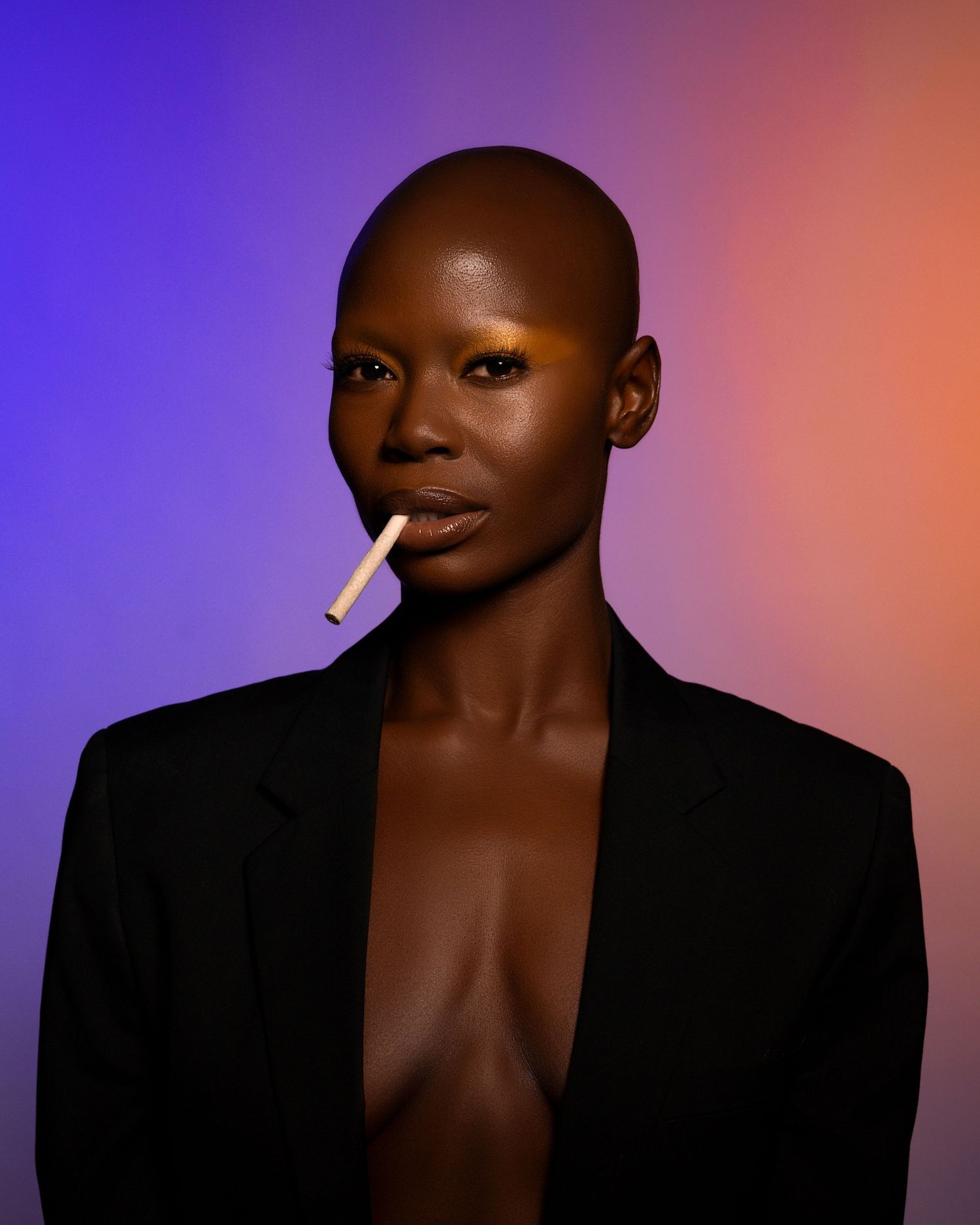 Fashion portrait against purple and orange gradient background featuring model in black blazer with cigarette.