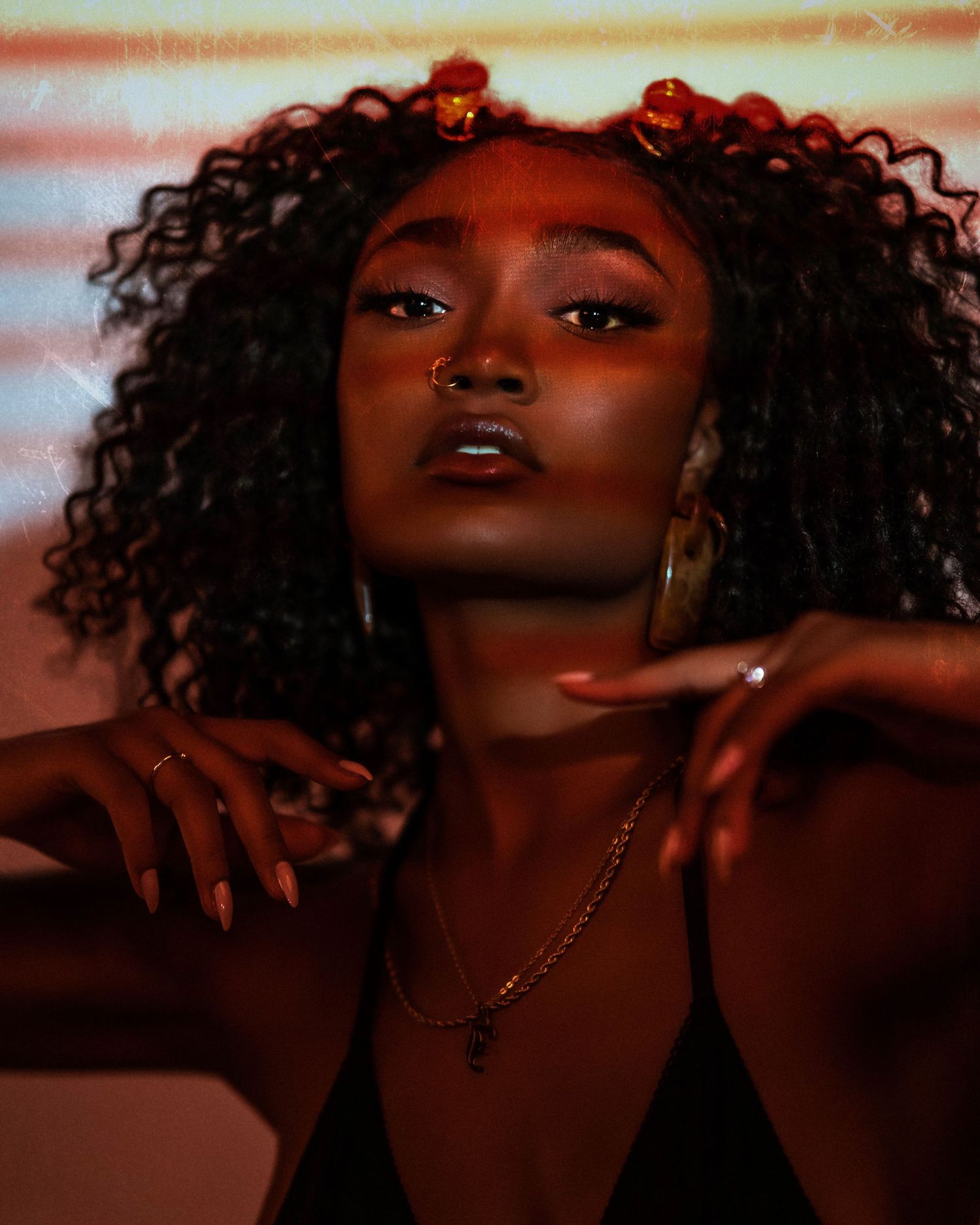 Artistic portrait series with warm lighting and natural curls against red-tinted background.