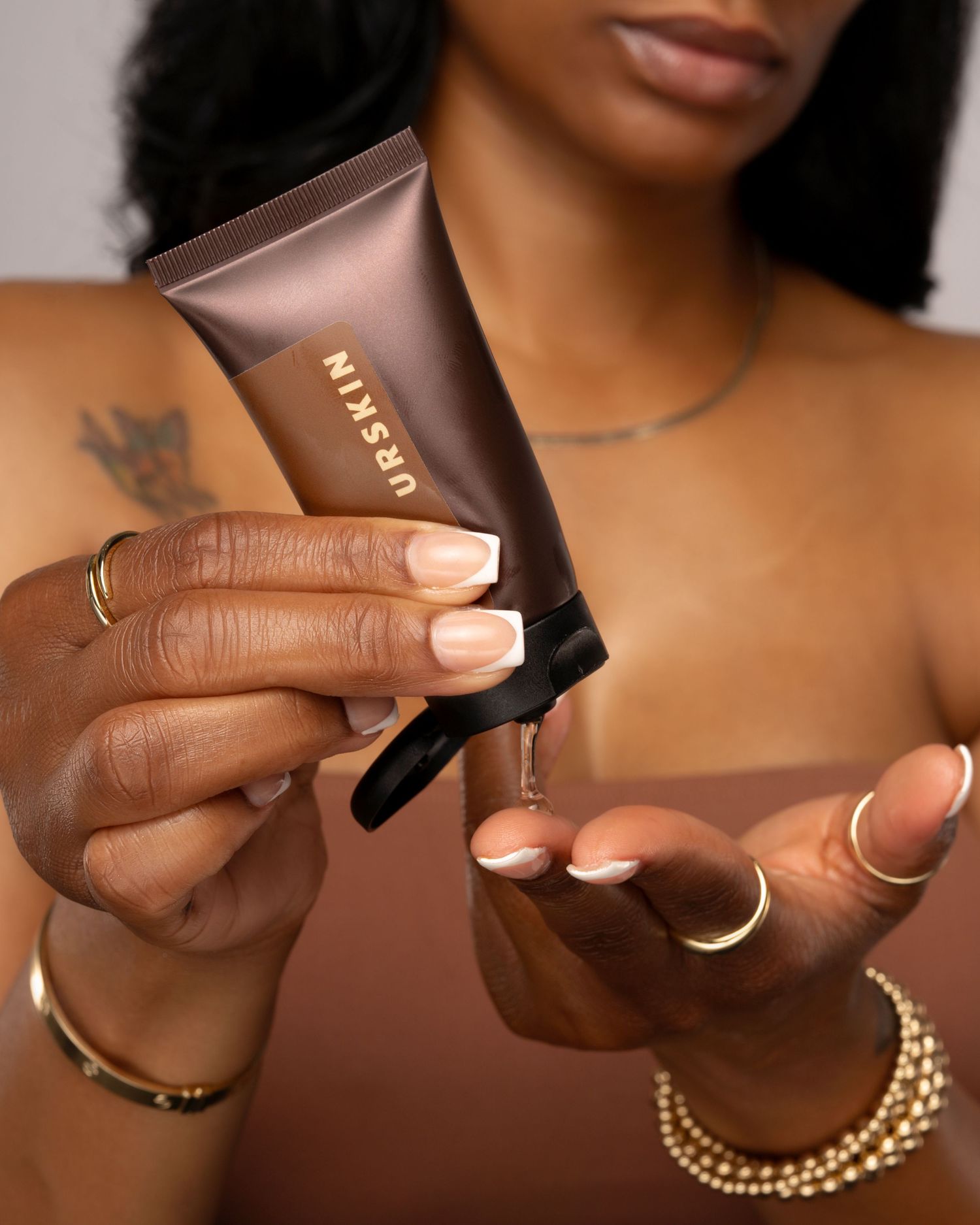 Hands holding bronze beauty product tube with jewelry accessories.