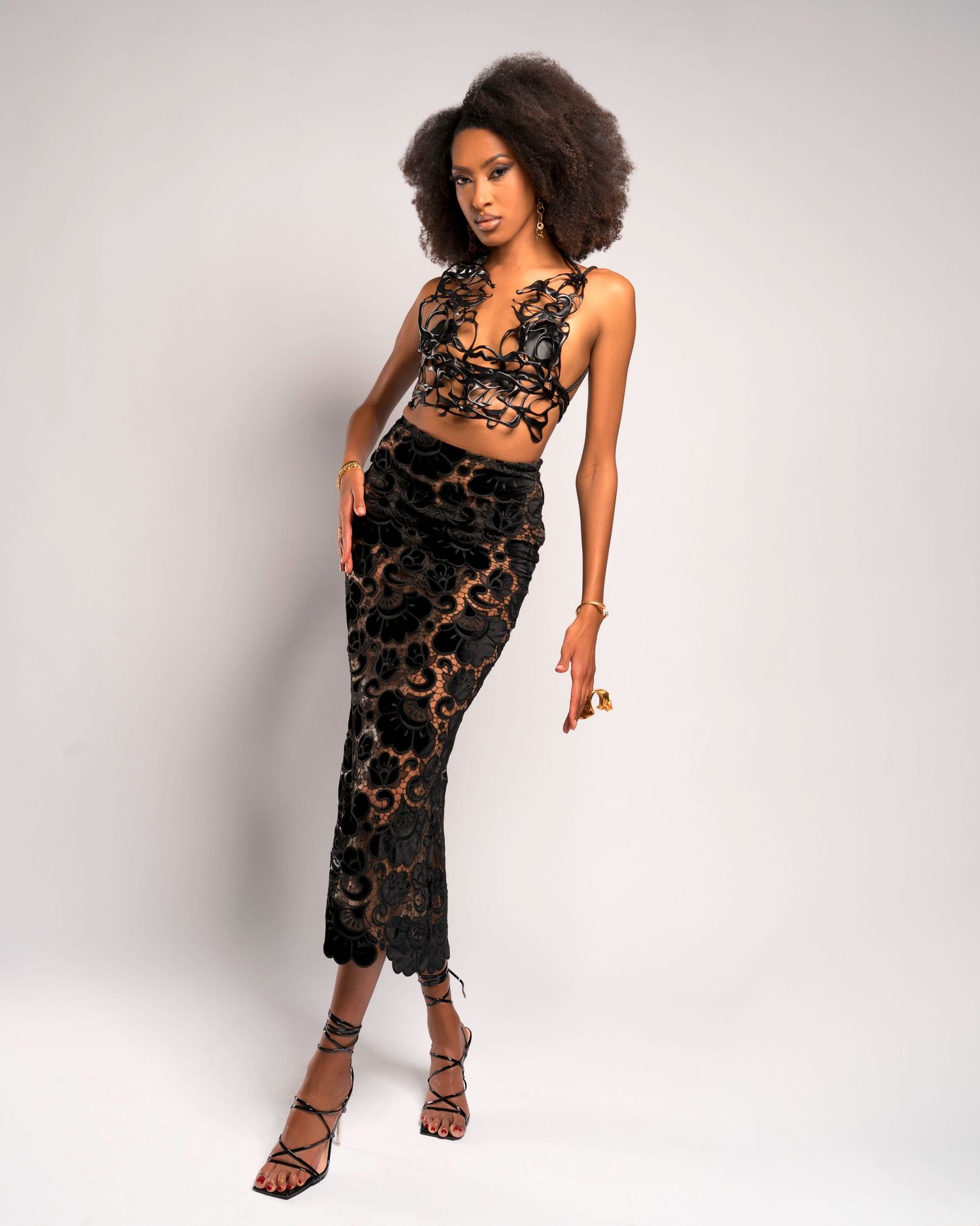 Fashion model wearing black lace two-piece outfit with crop top and midi skirt.