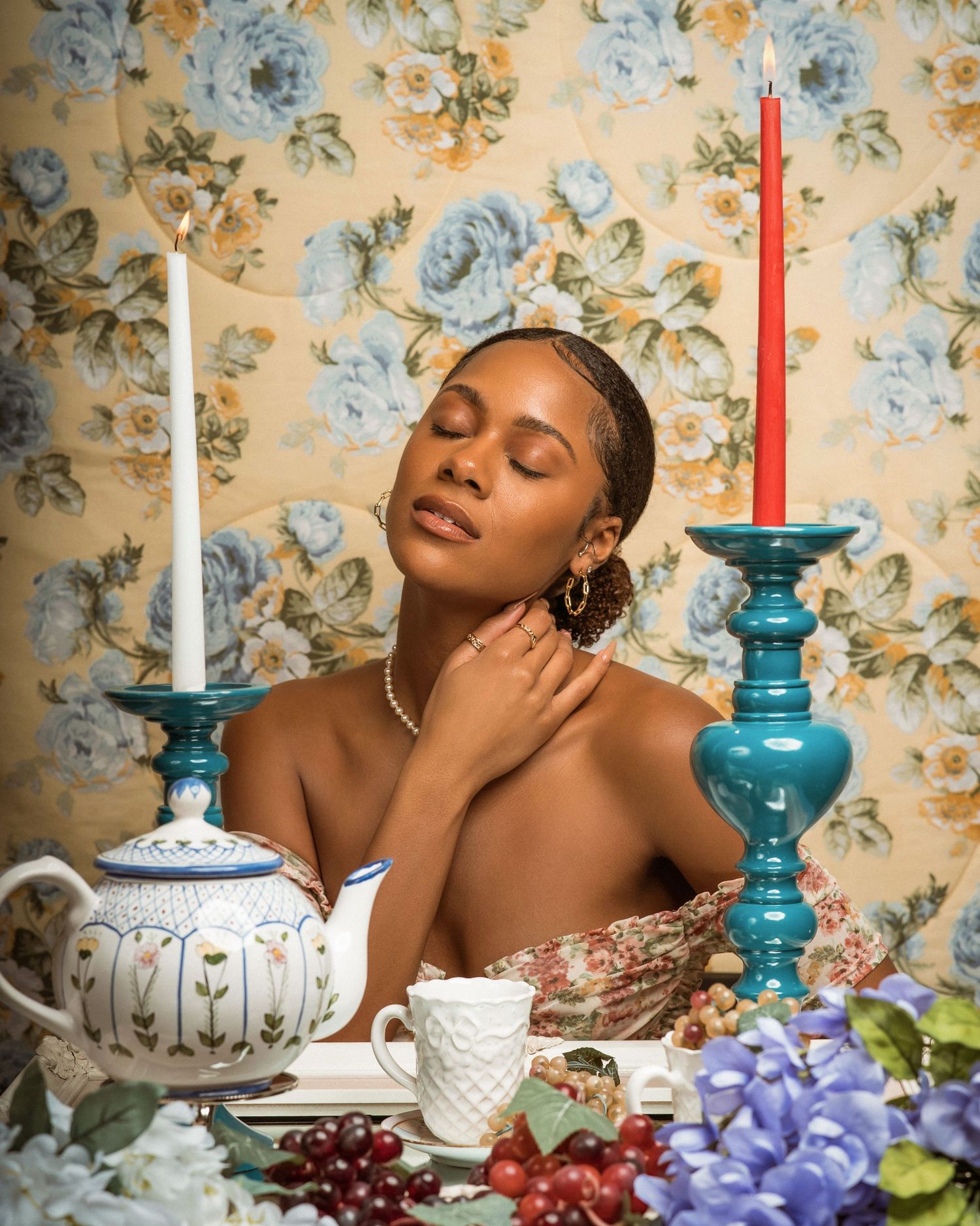 Dreamy tea party portrait with closed eyes, white candle, and blue floral wallpaper backdrop.