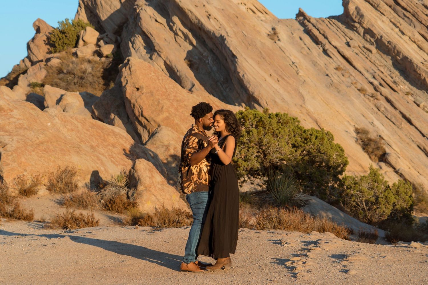 Couple embracing at sunset against dramatic red rock formations.