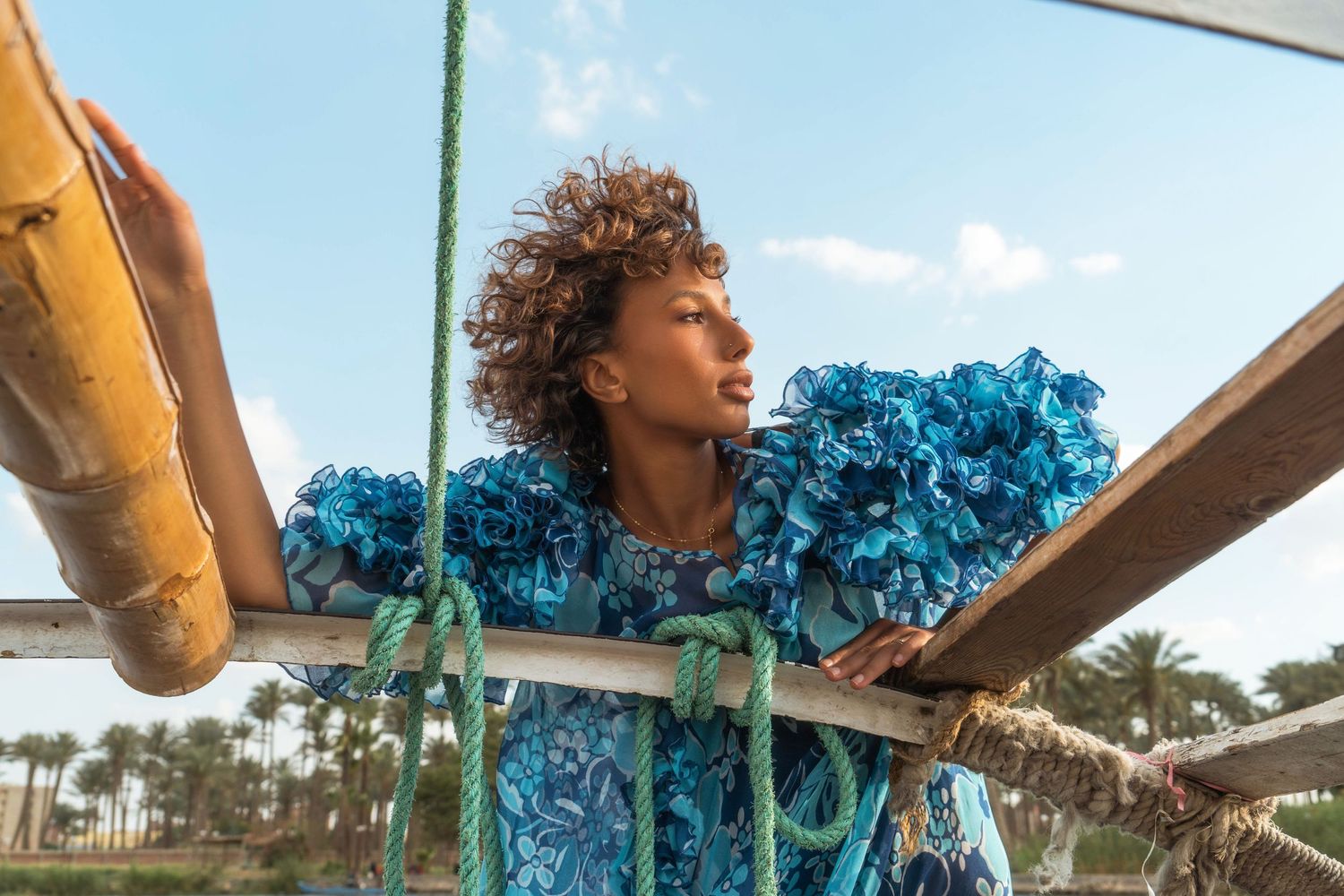 Person with curly hair laughing while sailing on boat against blue sky.