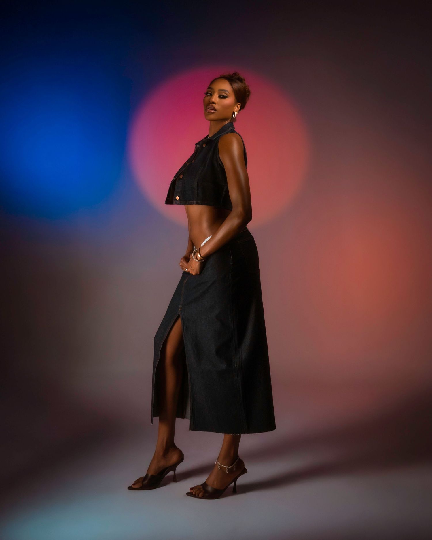 Artistic photoshoot with model in black dress against dramatic blue and red lighting.