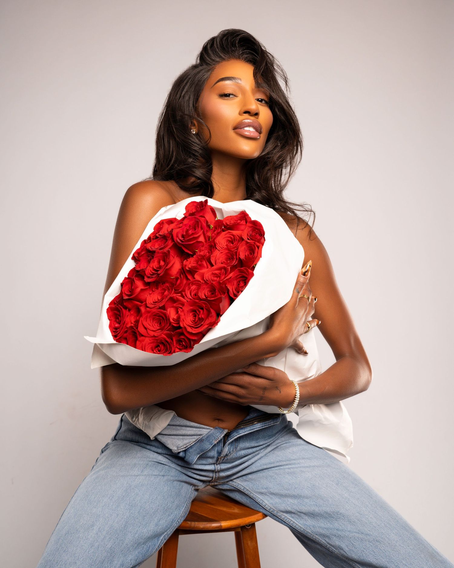 Fashion poses with model holding red rose bouquet wearing jeans on white backdrop.