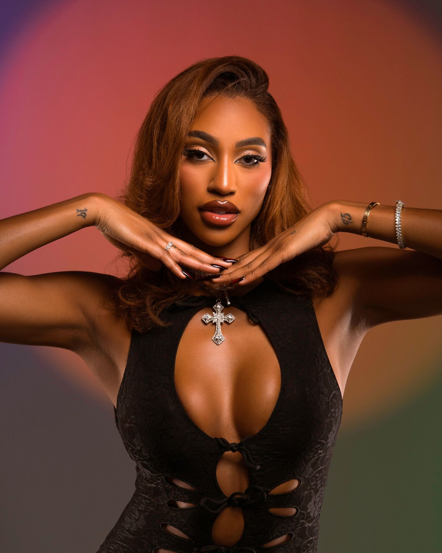Fashion model poses in black outfit with jewelry against colored gradient background.