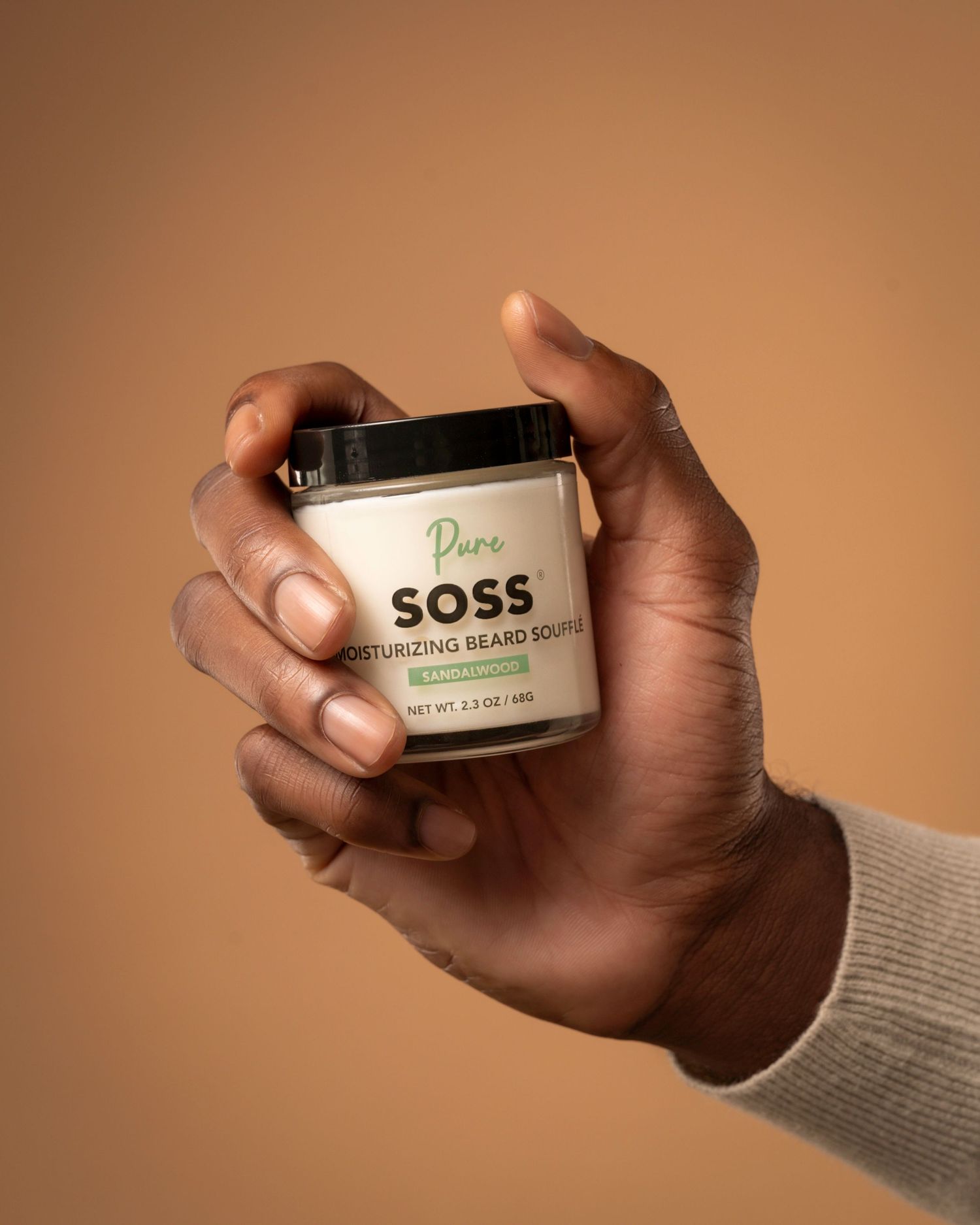 Hand holding a jar of SOSS moisturizing cream against warm brown backdrop.