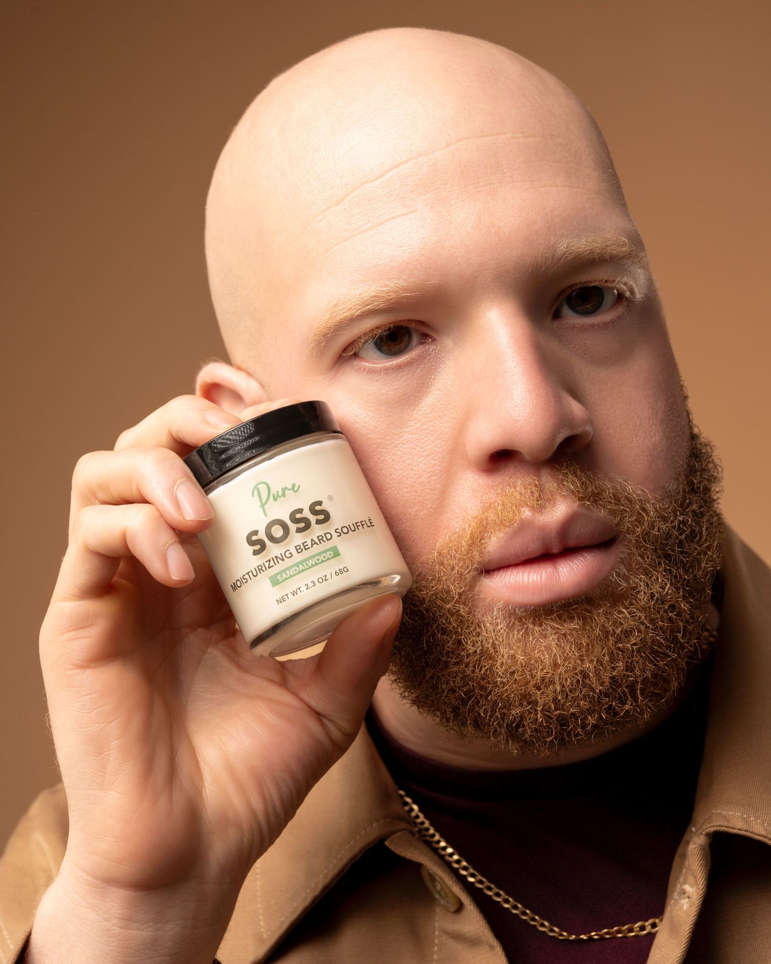Person holding a jar of SOSS skincare product against a brown background.