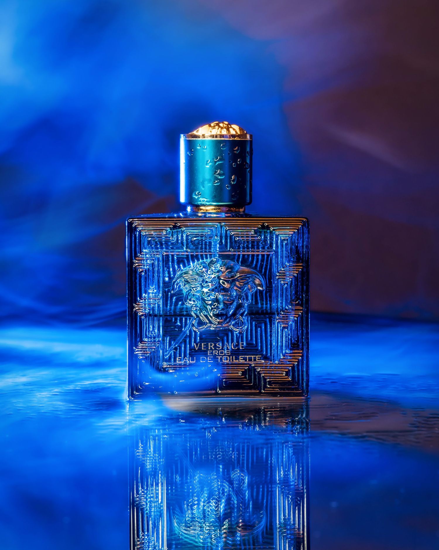 Blue perfume bottle with geometric pattern displayed on reflective surface.