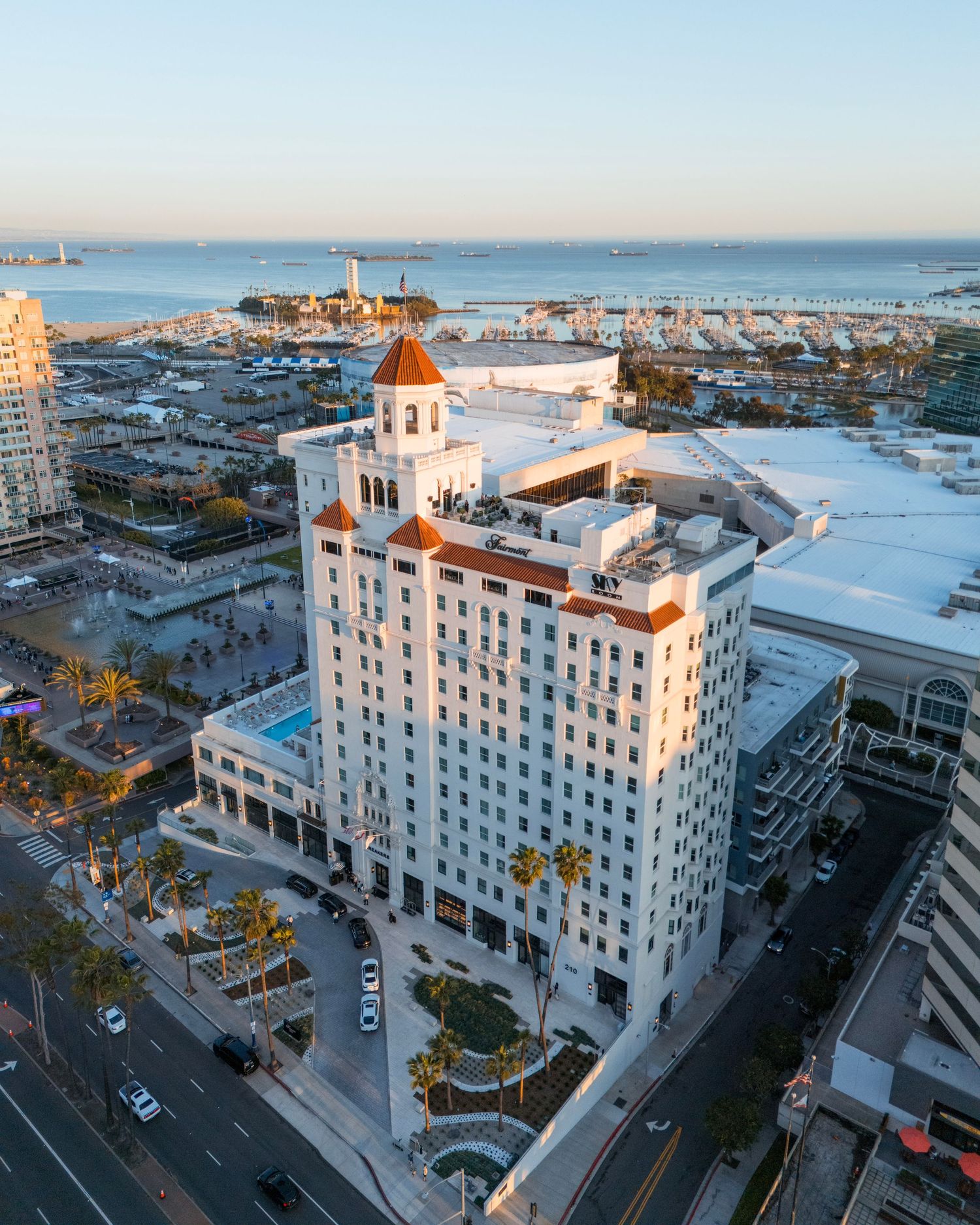Aerial panoramic view of a white historic hotel building with red dome towers in a coastal city setting at sunset.
