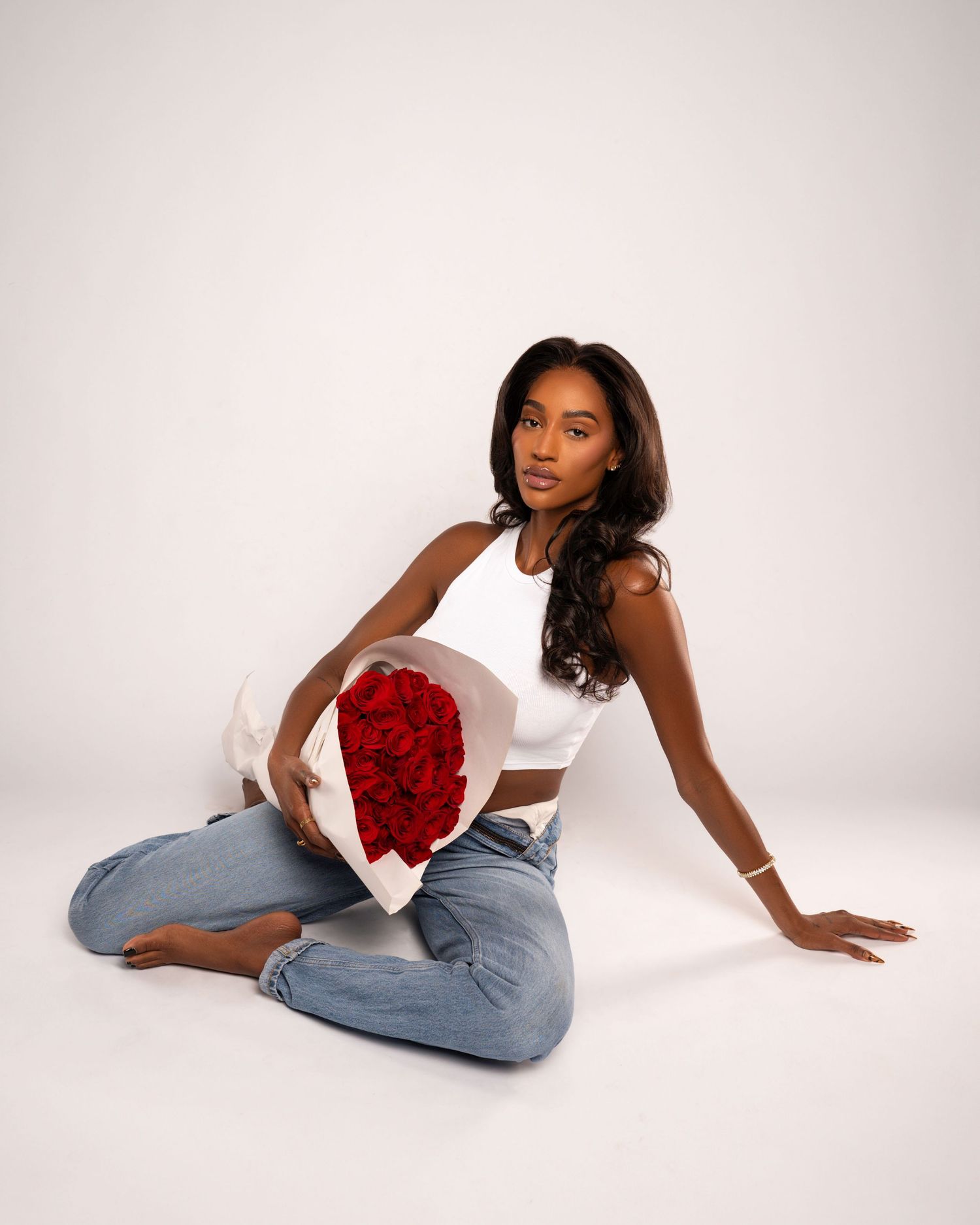 Casual portrait series with model in jeans holding red roses against white background.
