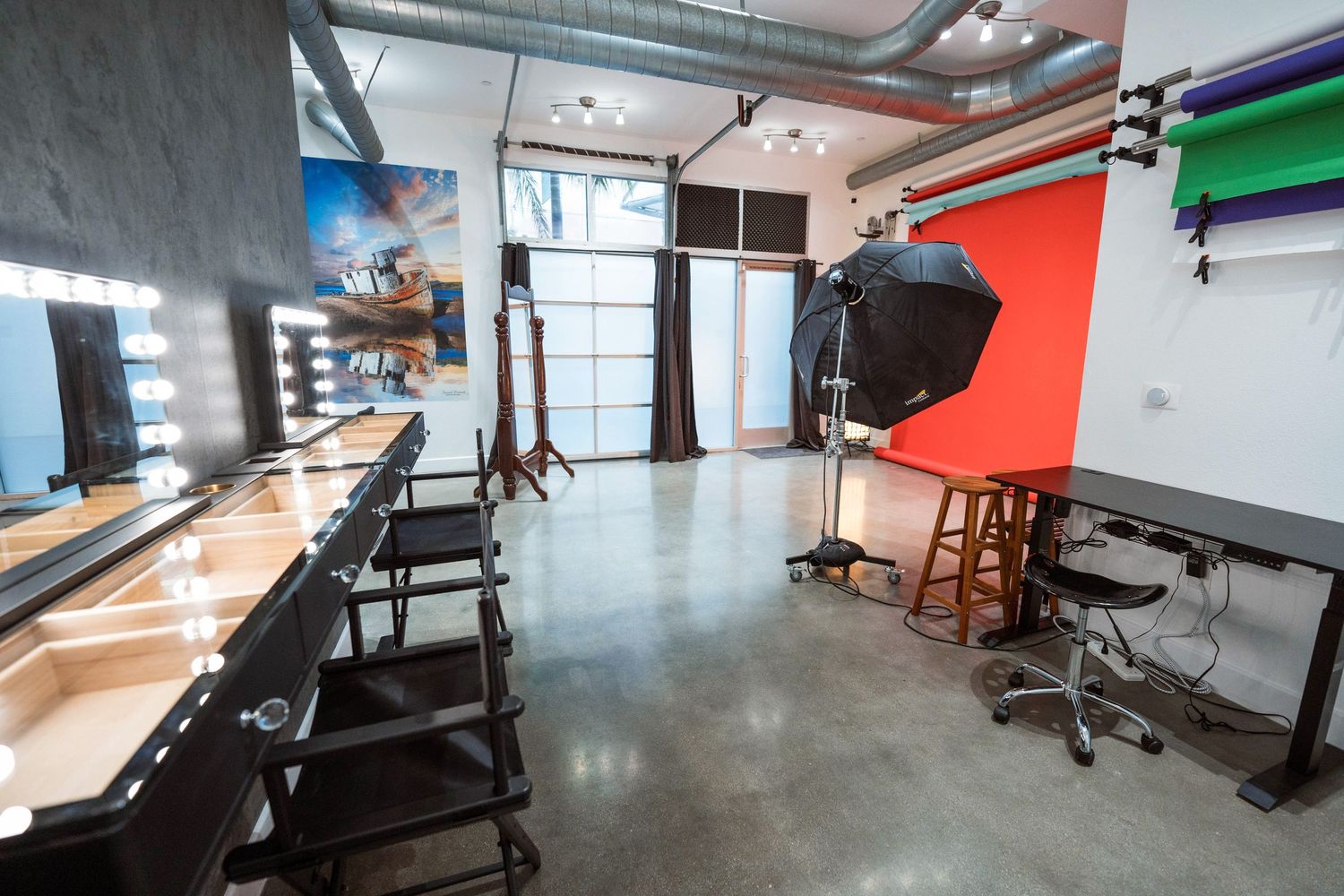 Professional photography studio with makeup vanity, octabox lighting, red backdrop, and polished concrete floors.