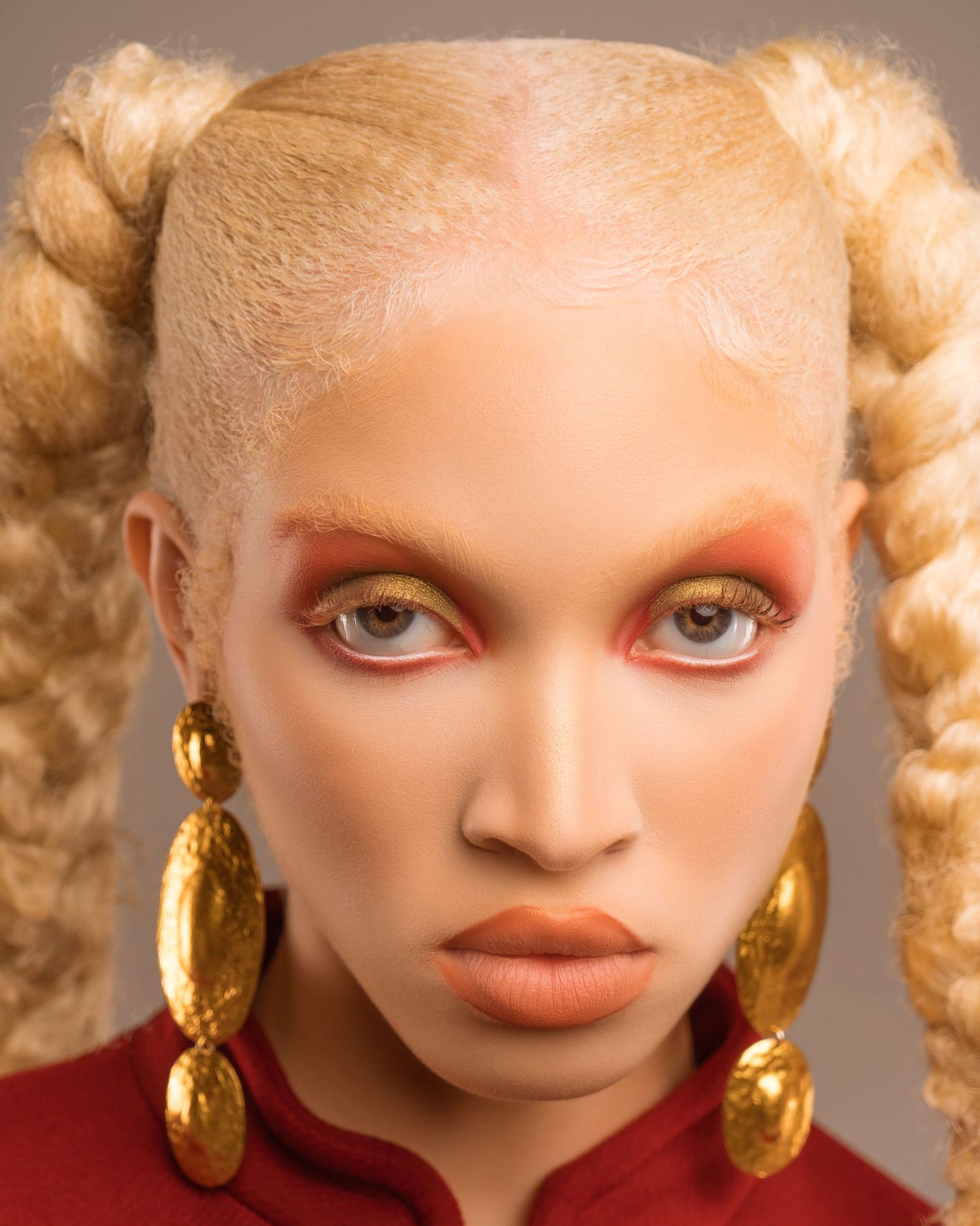 Close-up portrait of a model with pale features and gold earrings wearing dramatic makeup.