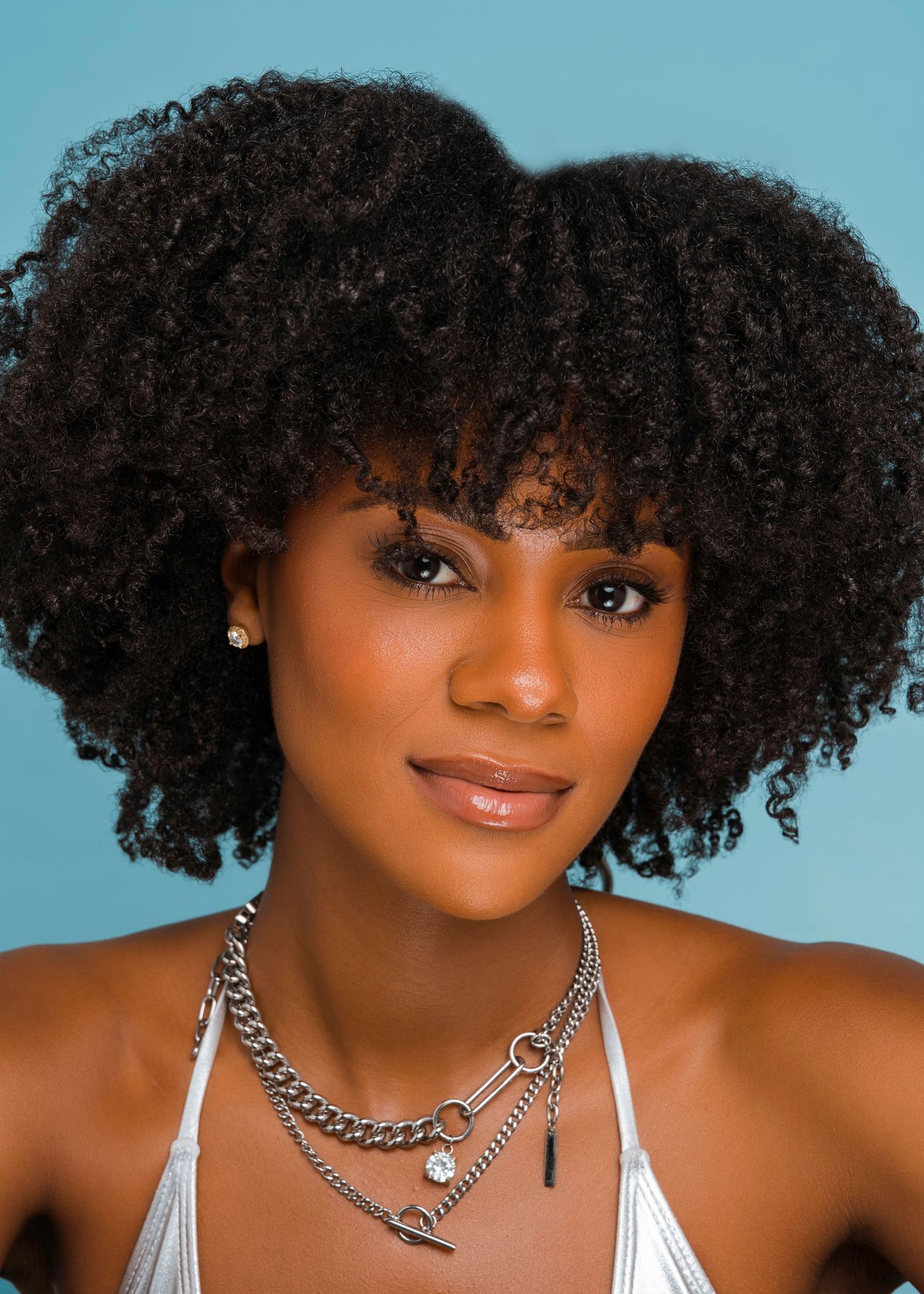 Fashion portrait series featuring silver chain necklace and natural curly hairstyle against blue backdrop.