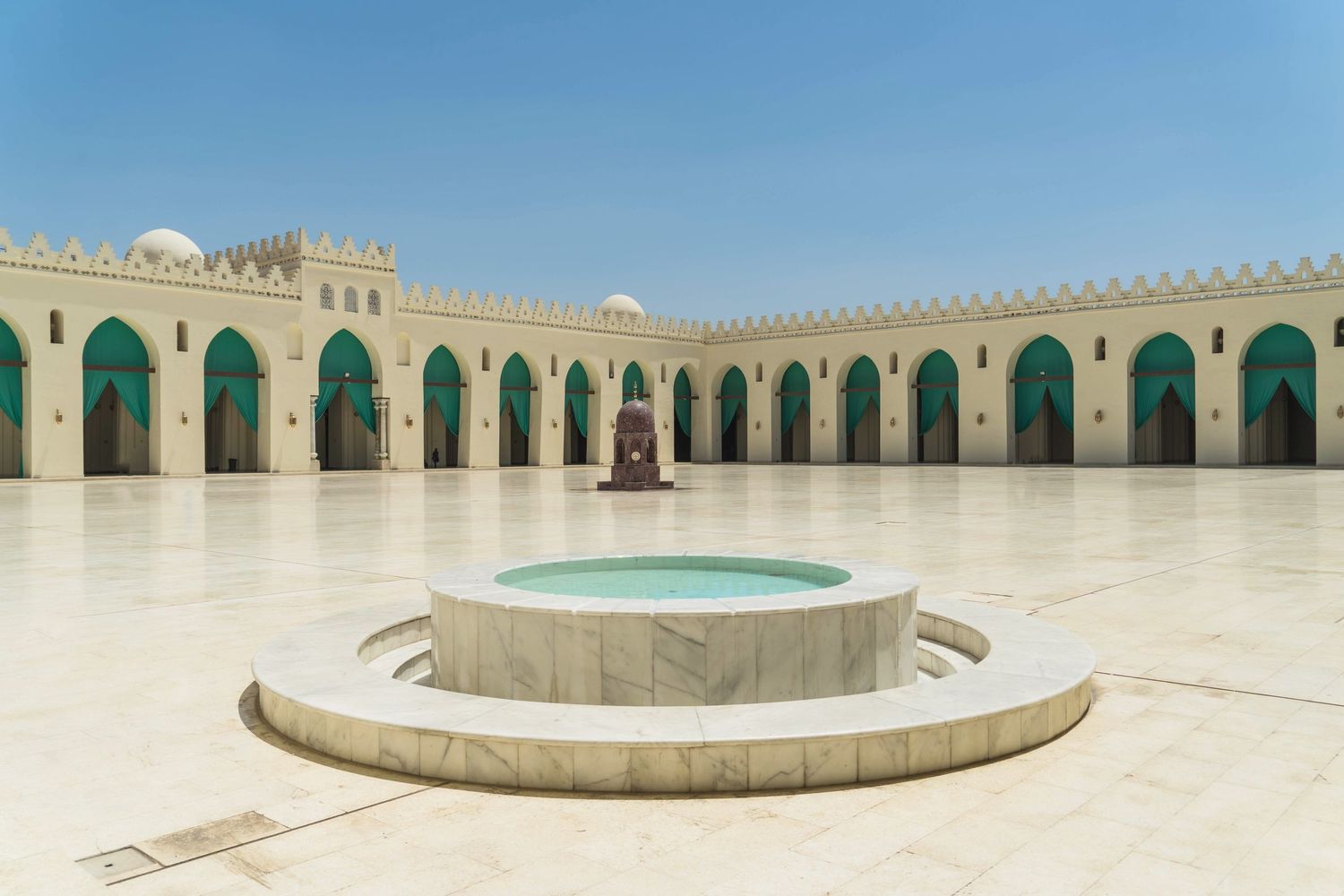 Panoramic view of ornate white mosque courtyard with decorative arches and pool.