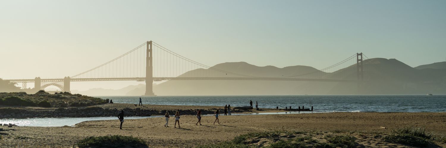 Wide panoramic view of the Golden Gate Bridge spanning San Francisco Bay under blue skies.